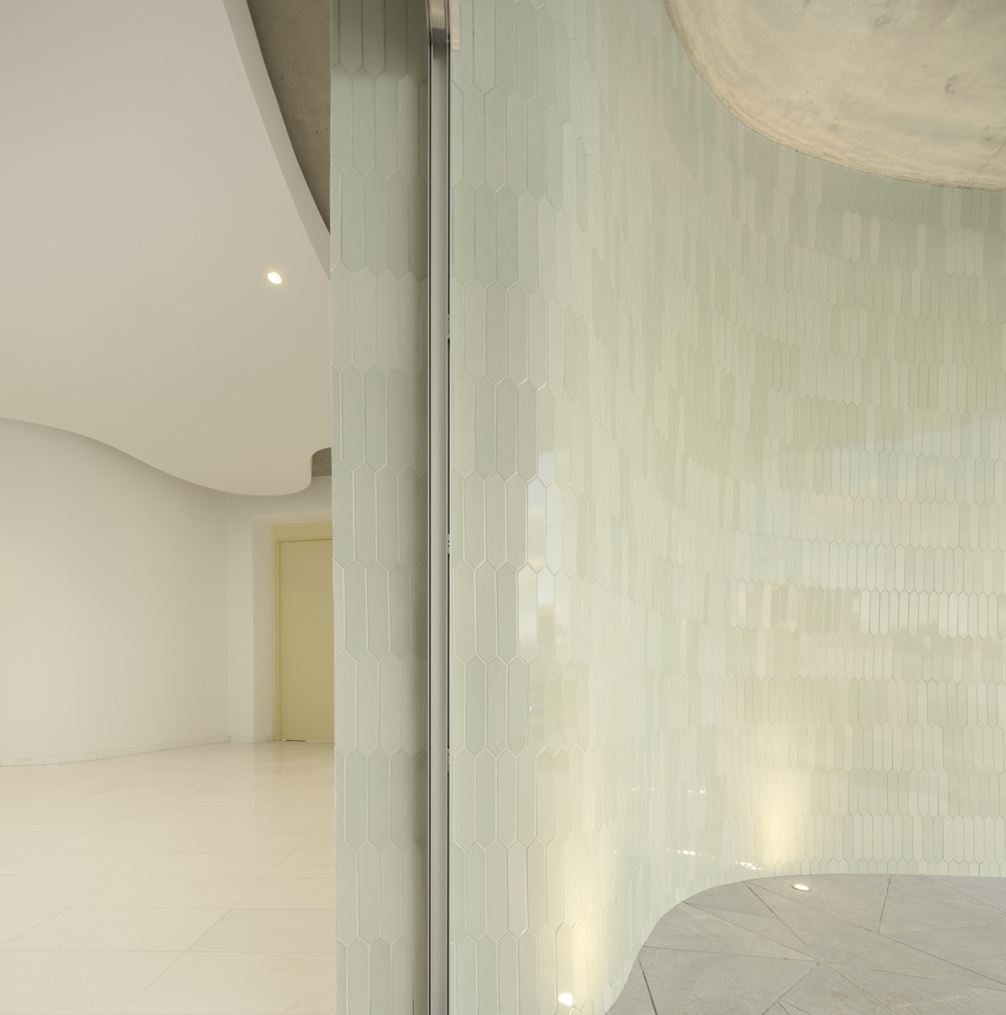 Translucent tiled partition wall separating curved interior volumes with soft natural light filtering through