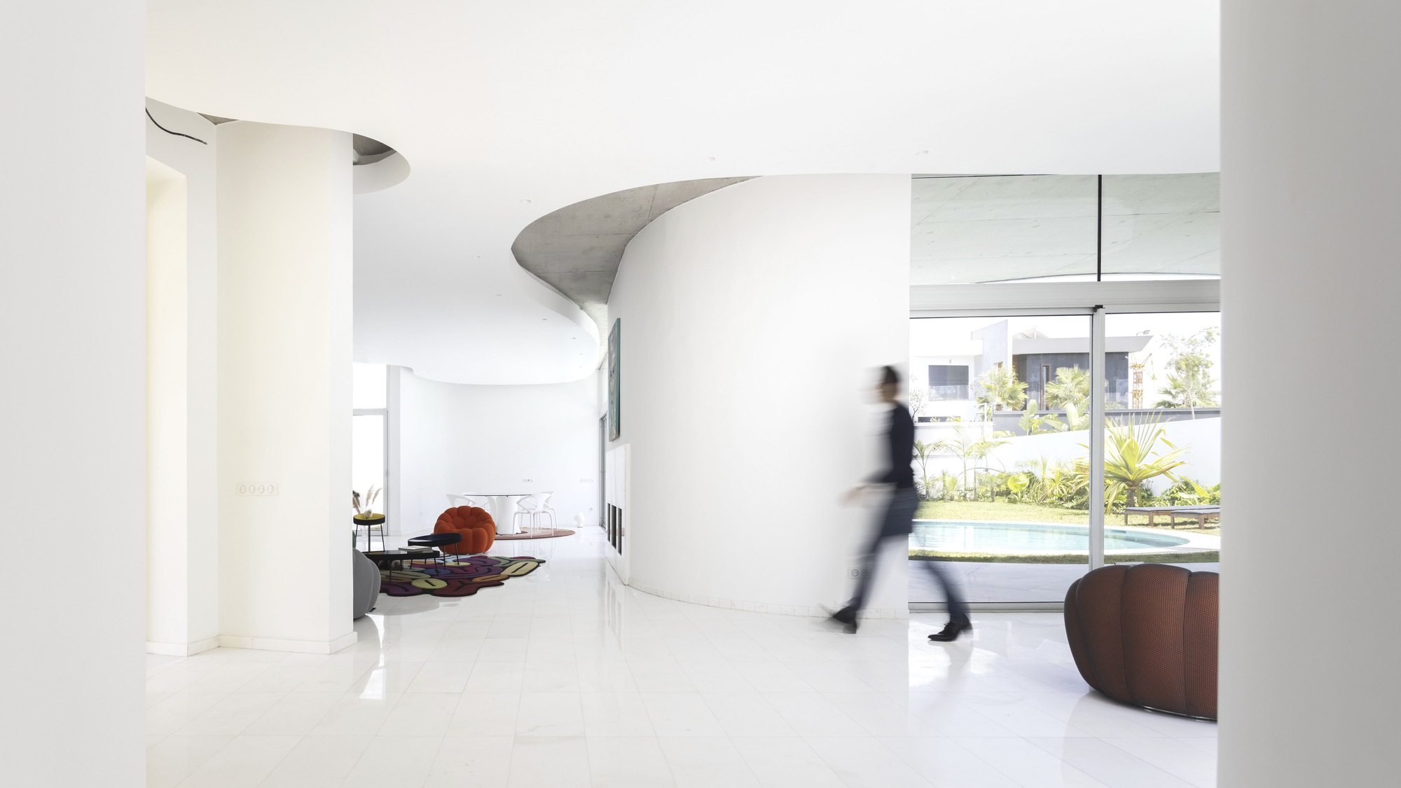 Open interior with white polished floors and a figure in motion passing a curved partition wall