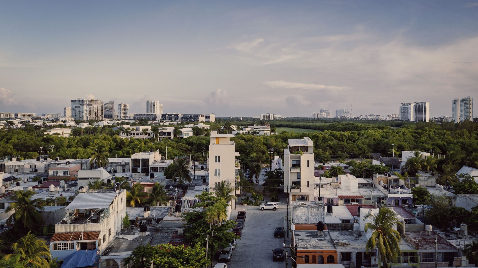 Aerial view of two white tower volumes rising above low-rise rooftops with distant high-rises on the horizon
