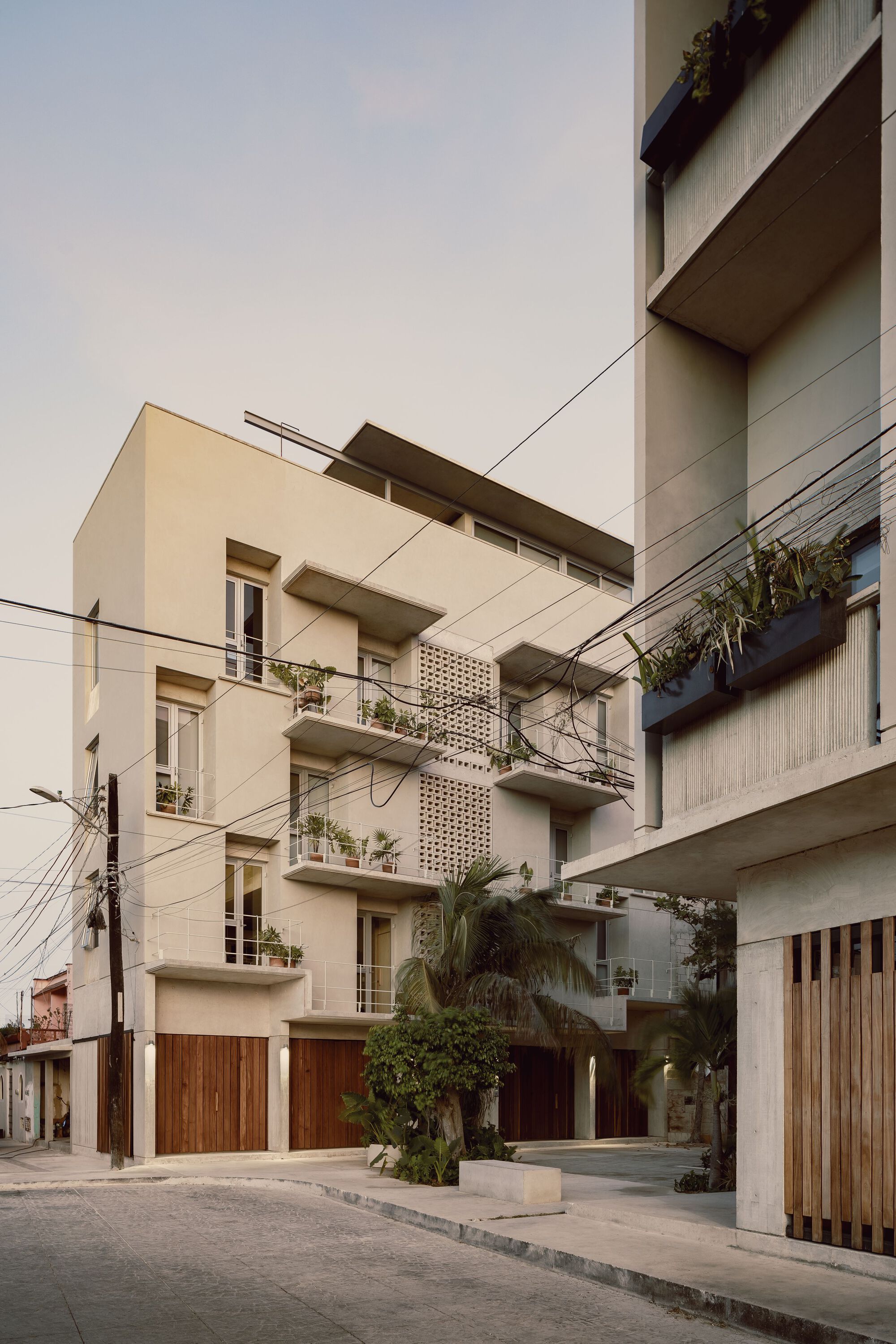 Street-level view of cream stucco facades with planted balconies and timber garage doors under overhead power lines