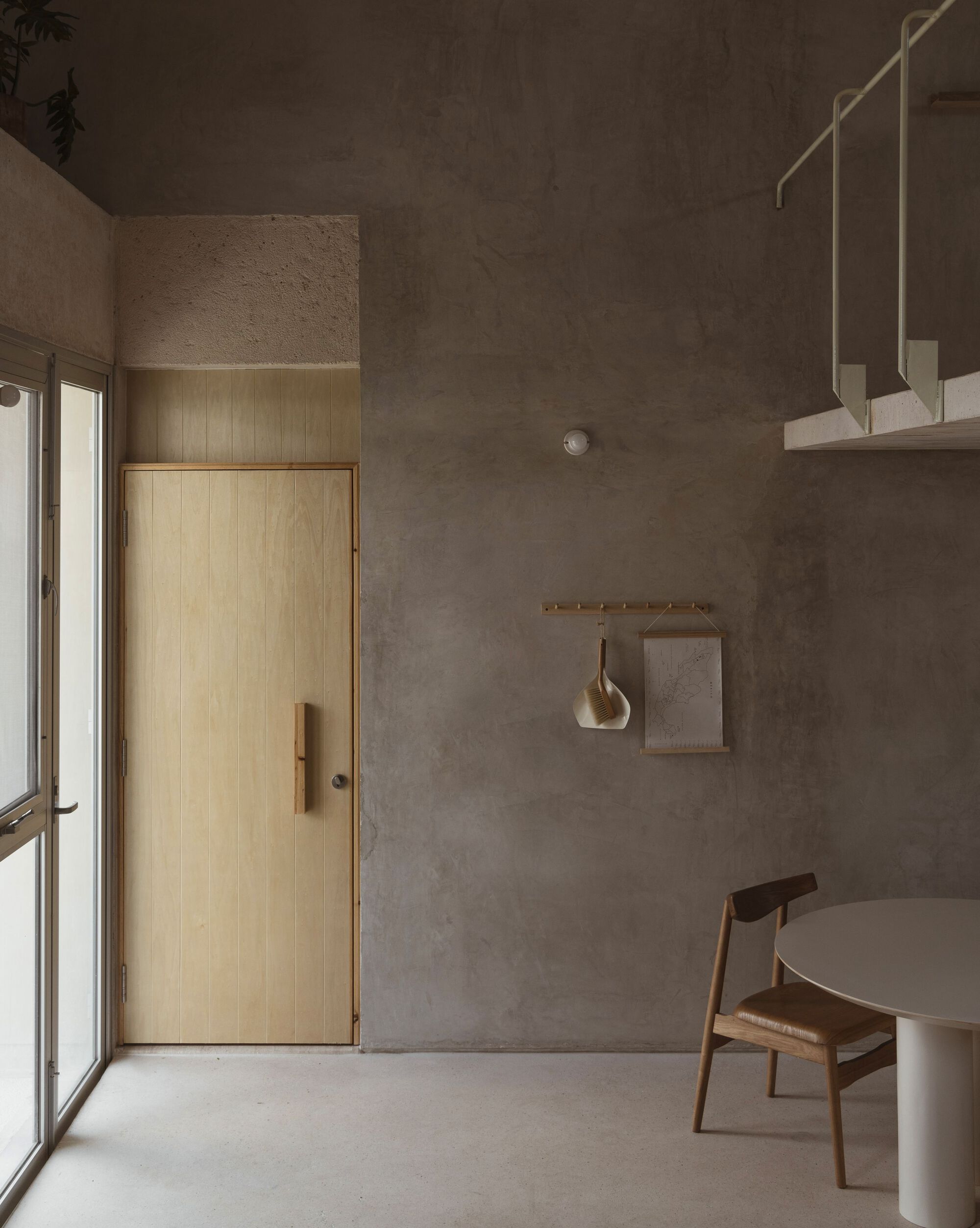 Interior room with raw concrete walls, timber door, suspended brass fixtures and polished concrete floor in soft light