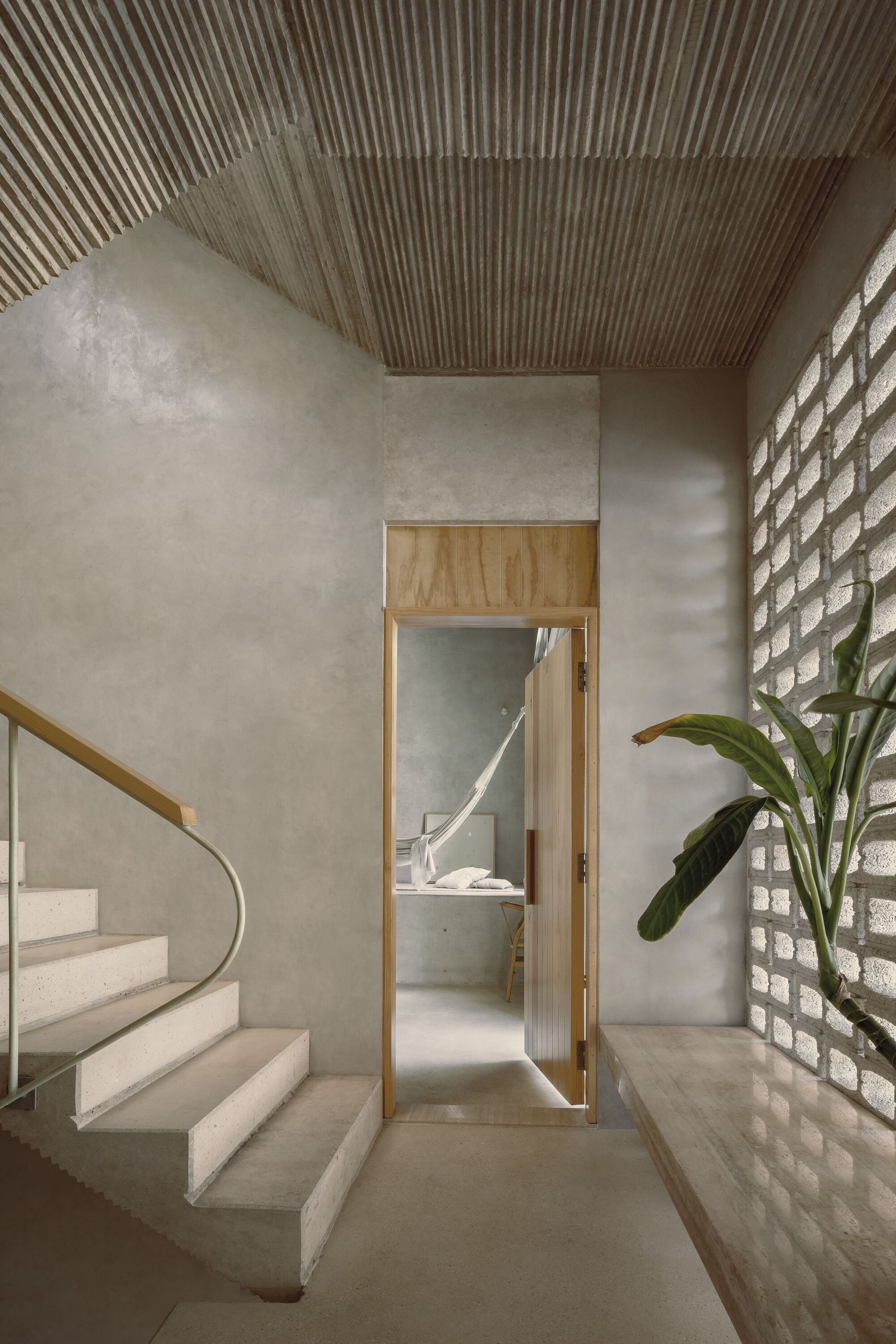 Concrete staircase with timber-framed doorway, corrugated ceiling and glass brick wall filtering daylight