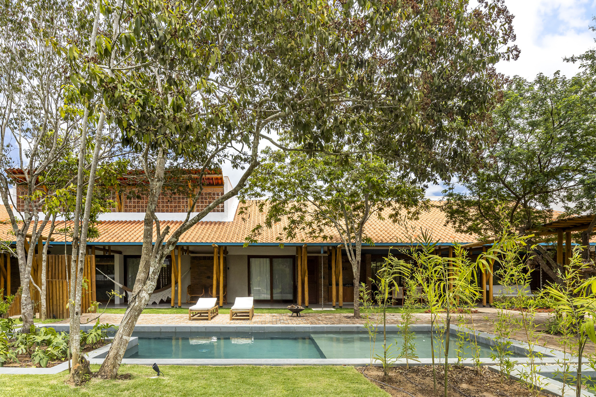 Rear facade with timber columns and tile roof overlooking a swimming pool framed by mature trees