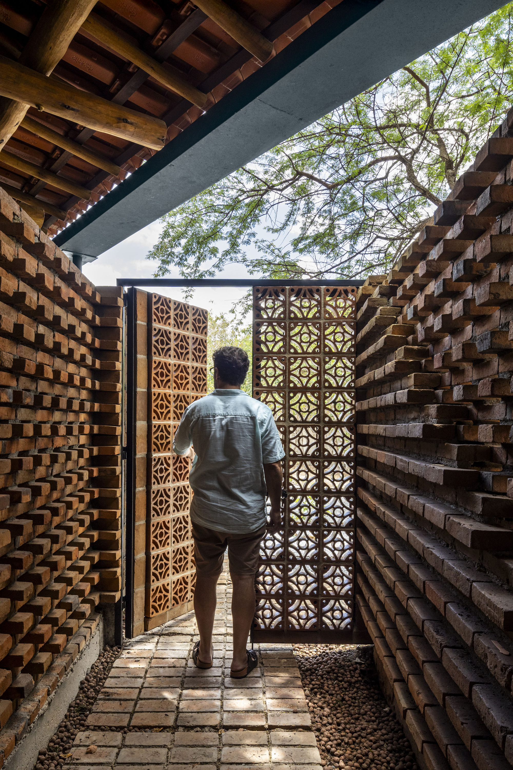 Person walking through brick-lined corridor toward patterned metal gate under a timber overhang