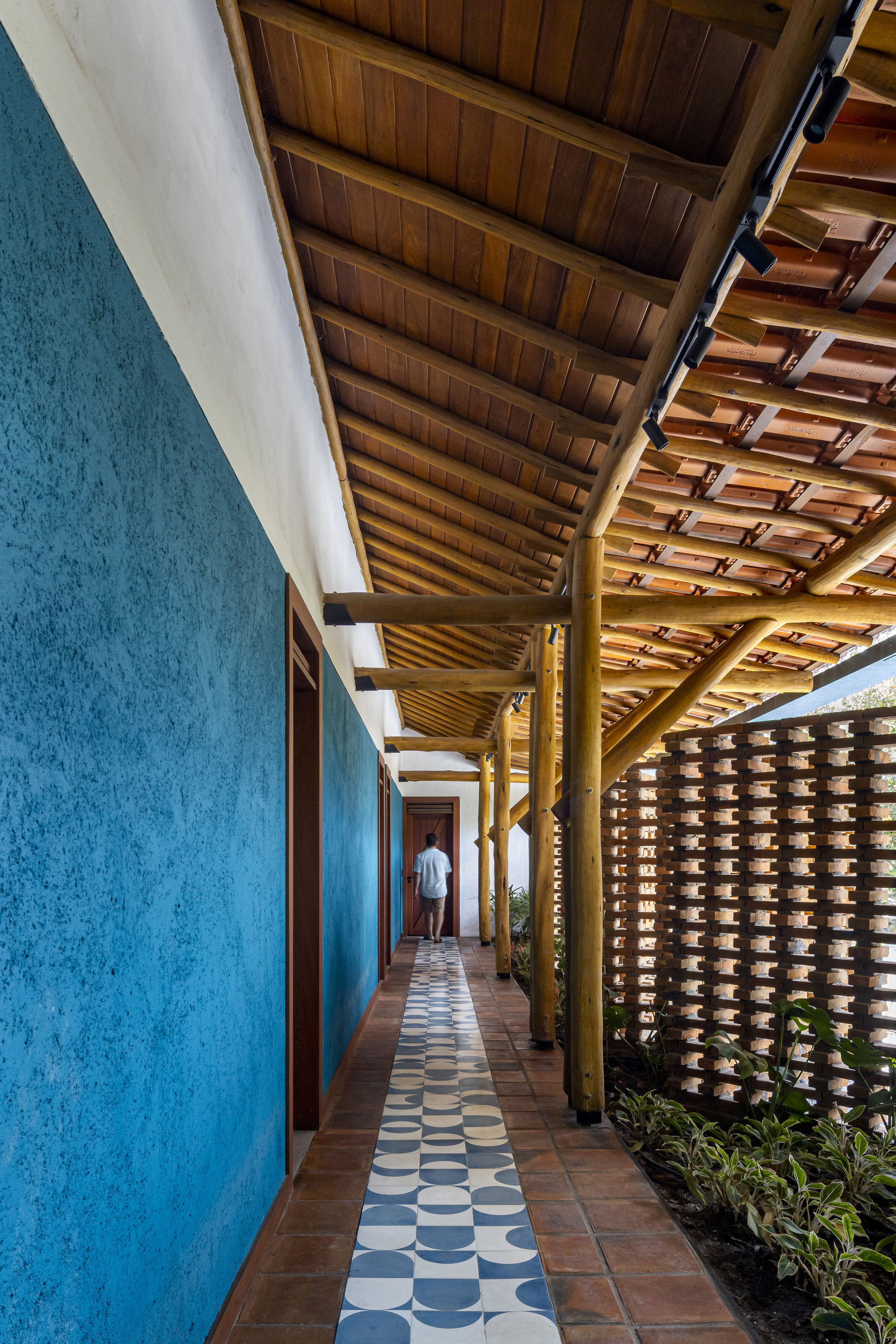 Covered walkway with blue plaster wall, patterned tile floor and perforated brick screen with plantings
