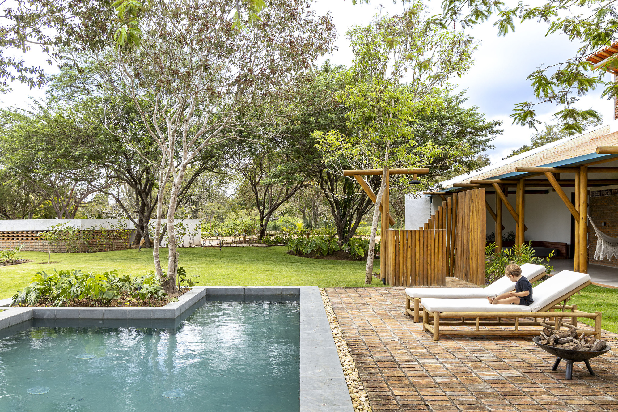 Pool terrace with brick pavers and wooden loungers beside a vertical timber screen and lawn