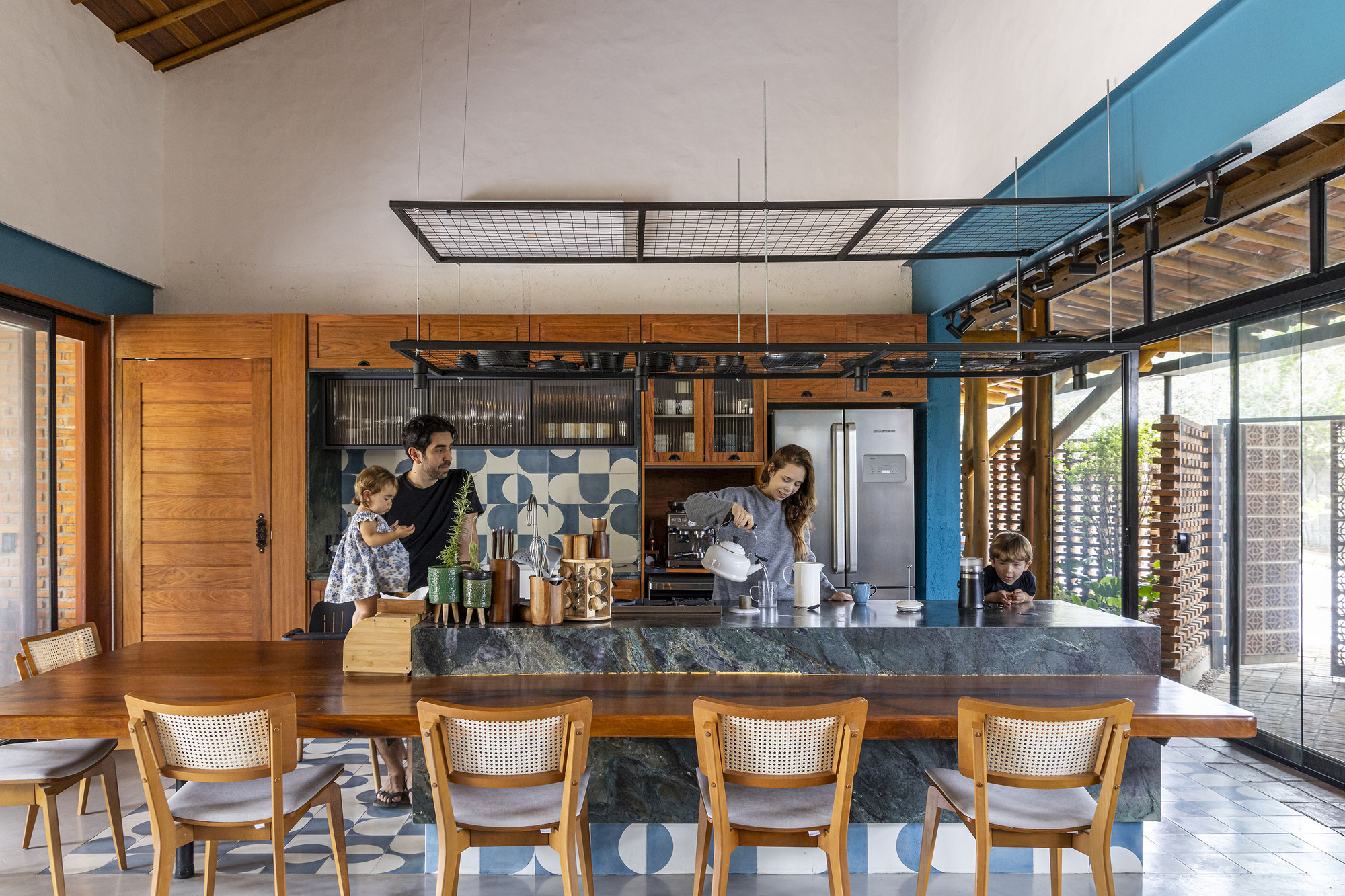 Kitchen island with dark stone countertop facing caned dining chairs under an exposed timber ceiling