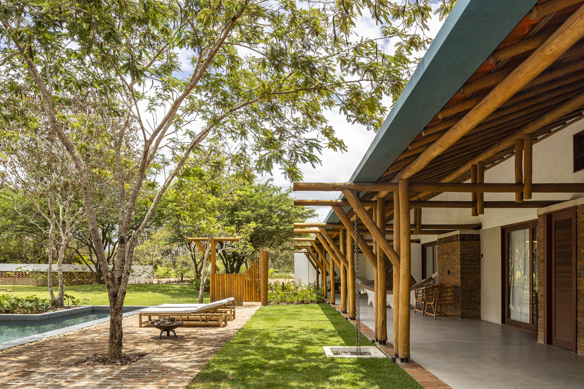 Covered porch with exposed timber rafters and beams overlooking a lawn shaded by mature trees