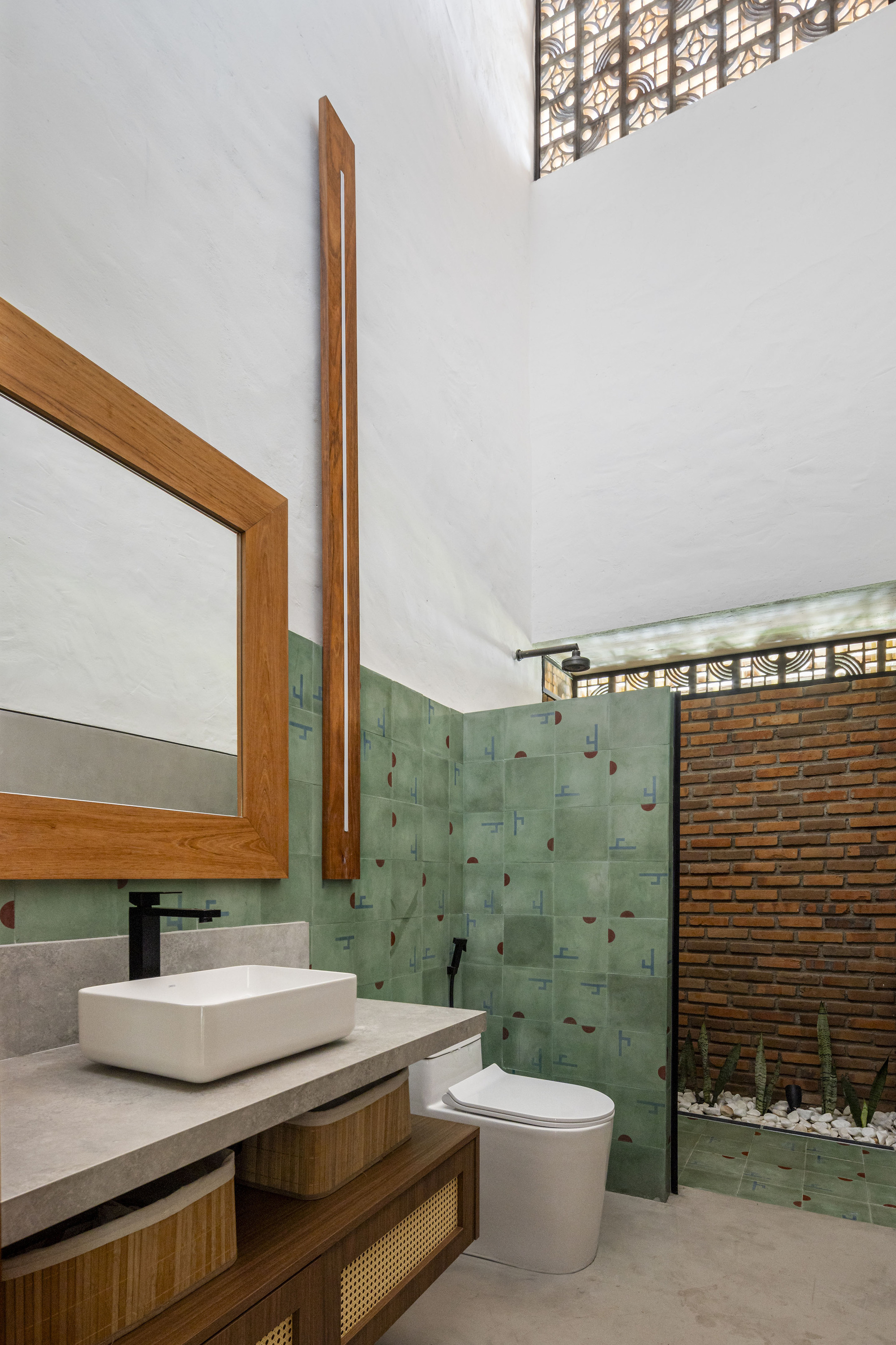 Bathroom with green tile accent wall, timber-framed mirror, and glass shower screen opening to courtyard