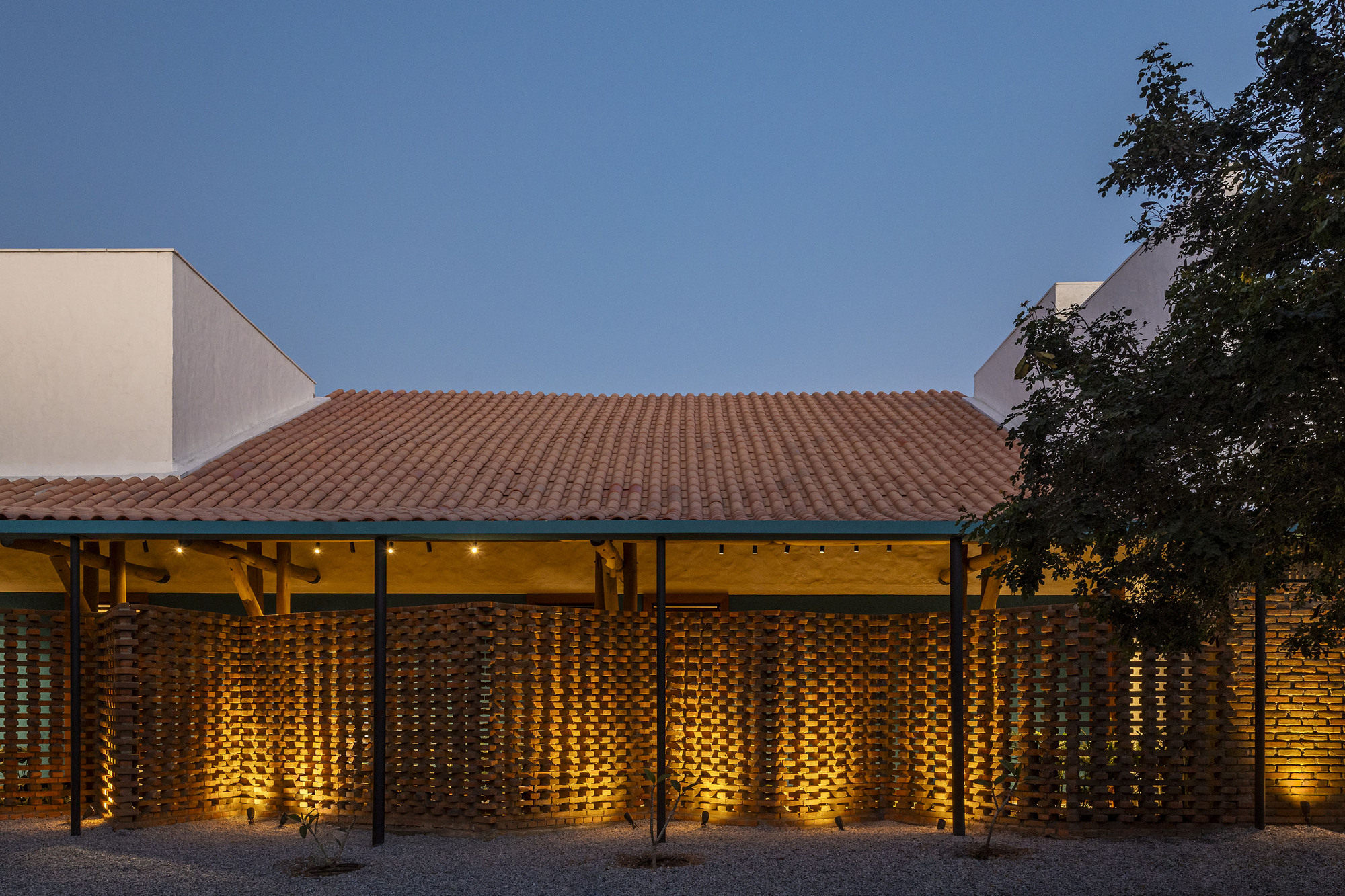 Clay tile roof and illuminated perforated brick screen facade beneath timber eaves at twilight