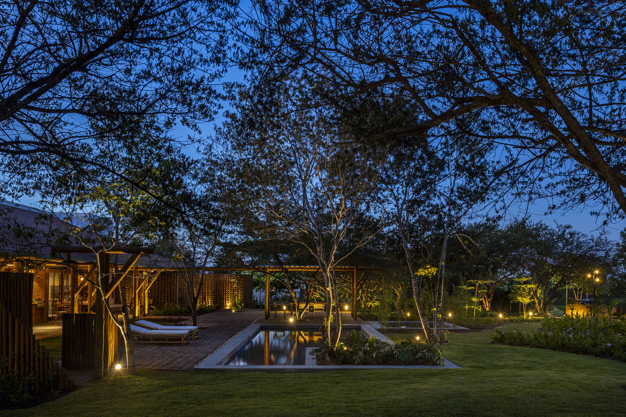 Garden courtyard with rectangular reflecting pool surrounded by timber pavilions and uplighted trees at twilight