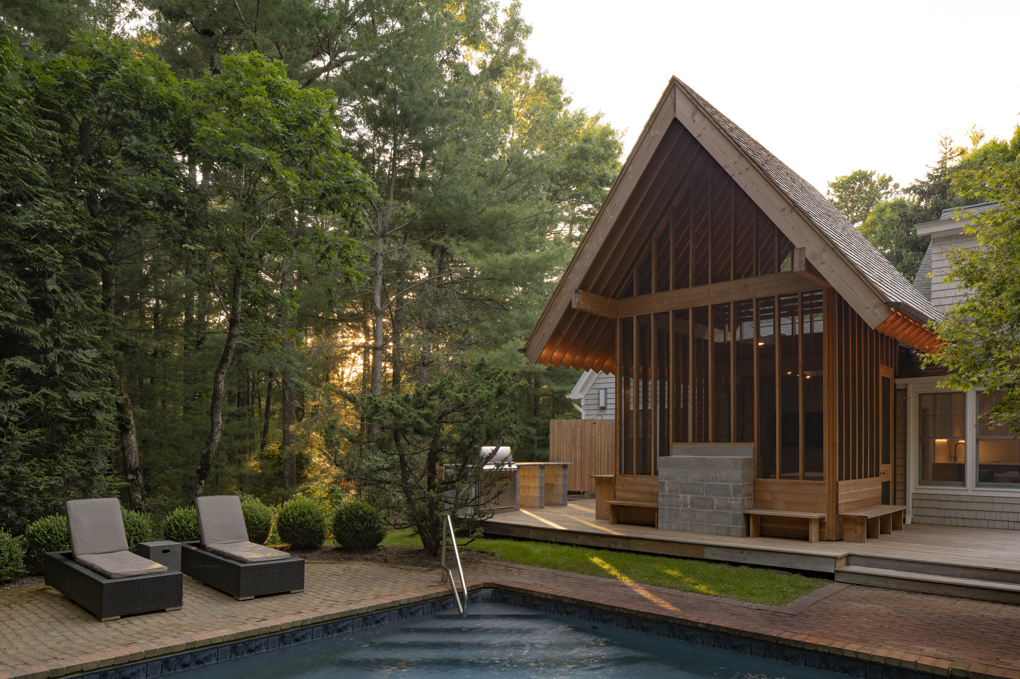 Poolside view of the timber pavilion with concrete block base and surrounding forest at sunset