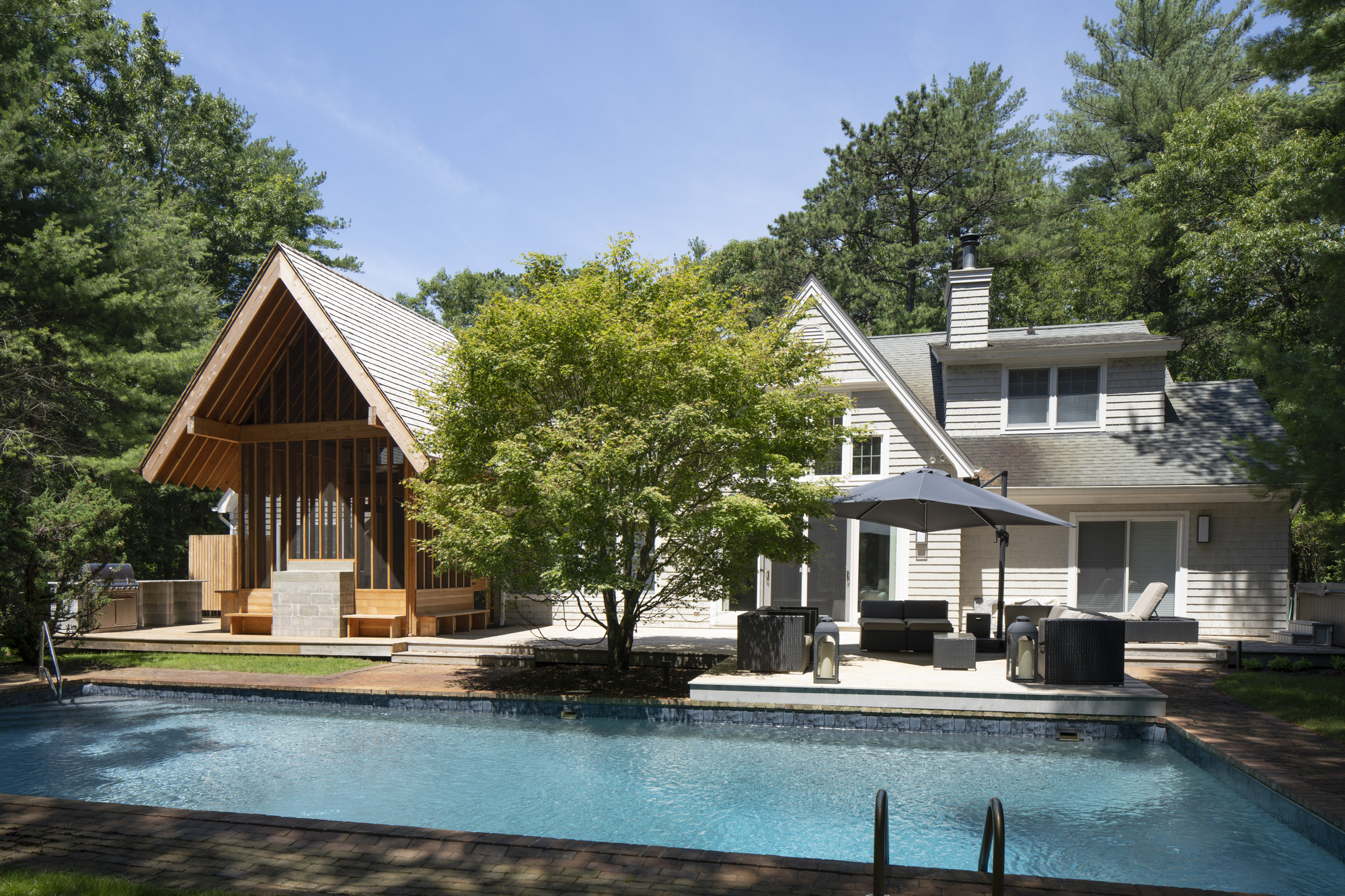 Pool terrace with open-air pavilion and white clapboard residence framed by mature trees