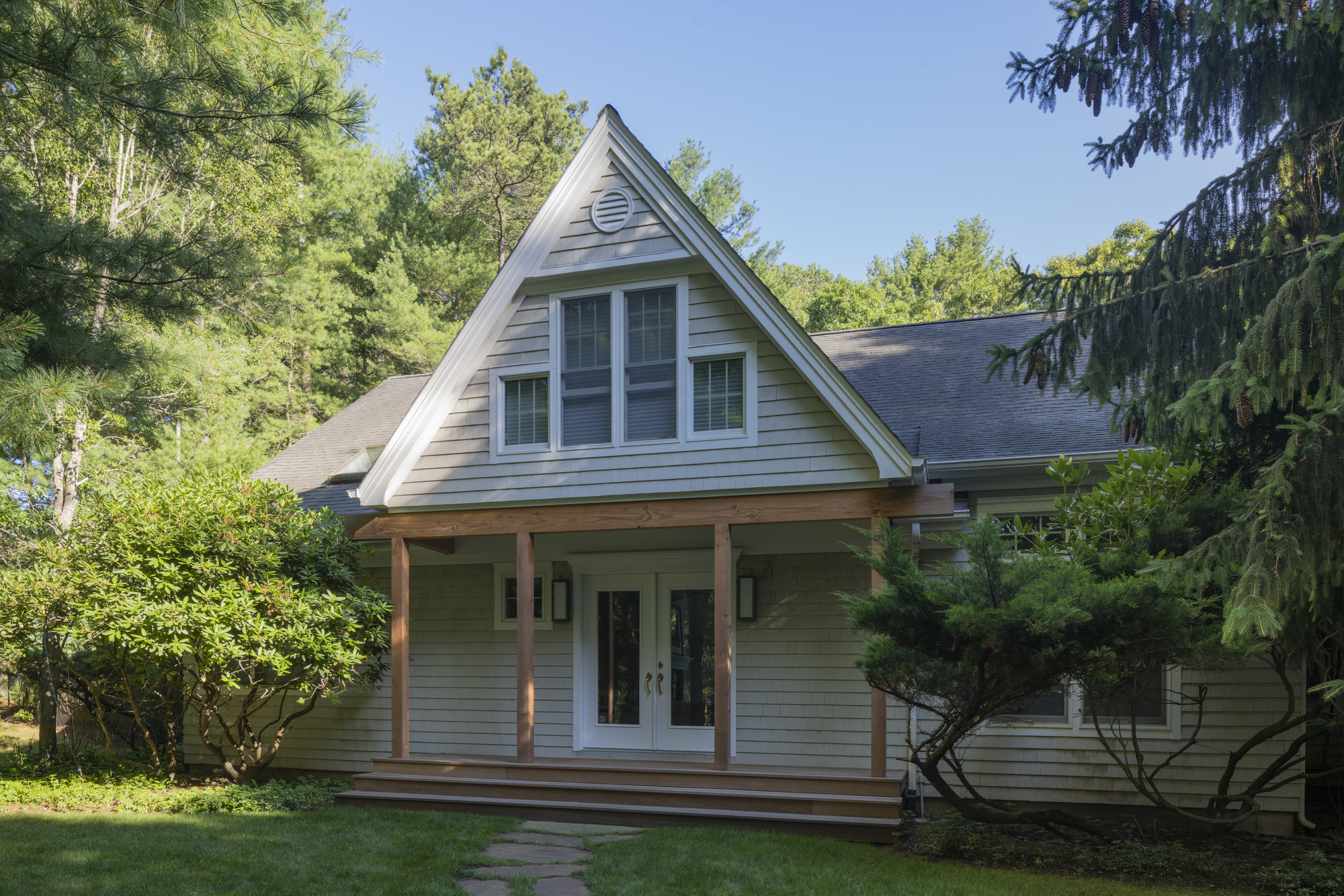 Front porch with timber columns and triangular gable vent beneath a clear summer sky