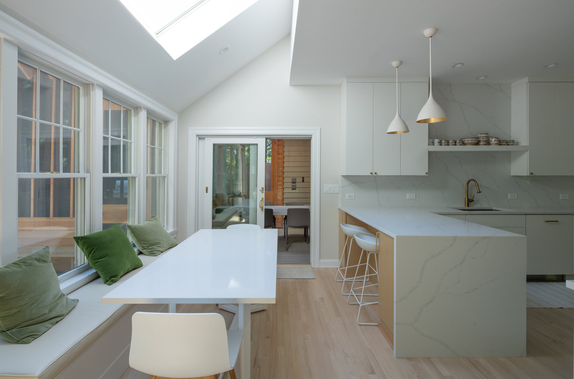 White kitchen with island and pendant lights adjacent to a window seat flooded with daylight