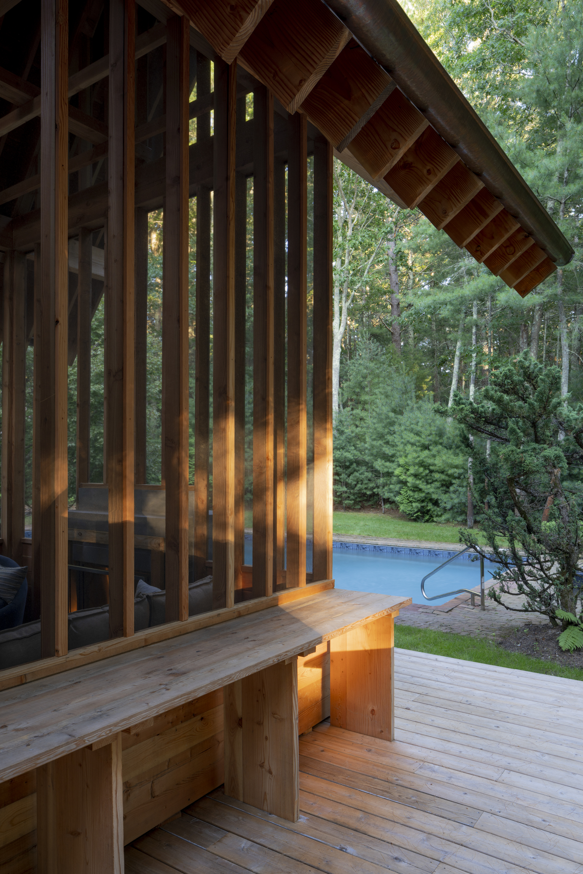 Corner detail of the vertical timber screen with built-in bench at dusk beside the pool