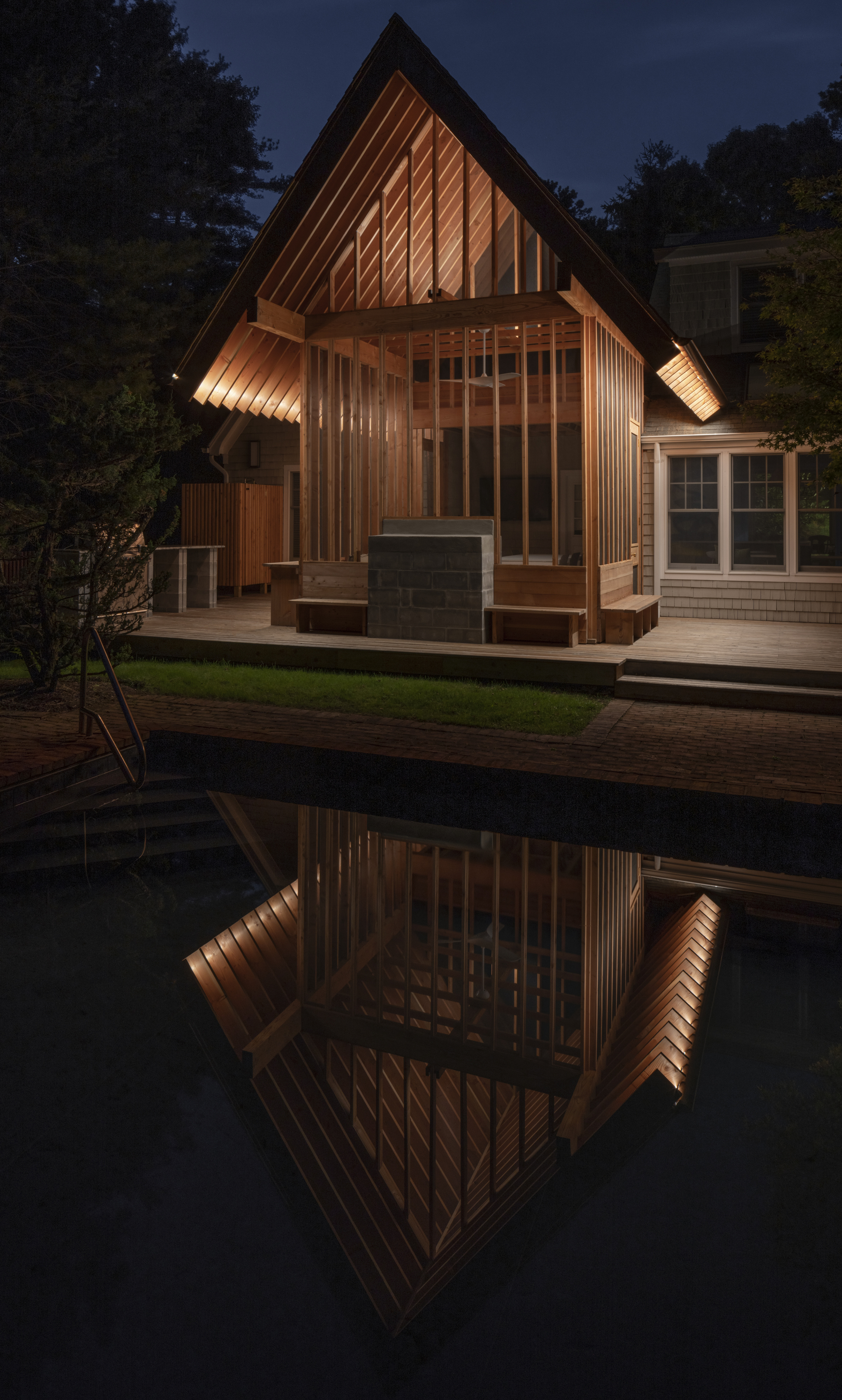 Poolside pavilion with gabled roof and vertical timber cladding reflected in still water at twilight