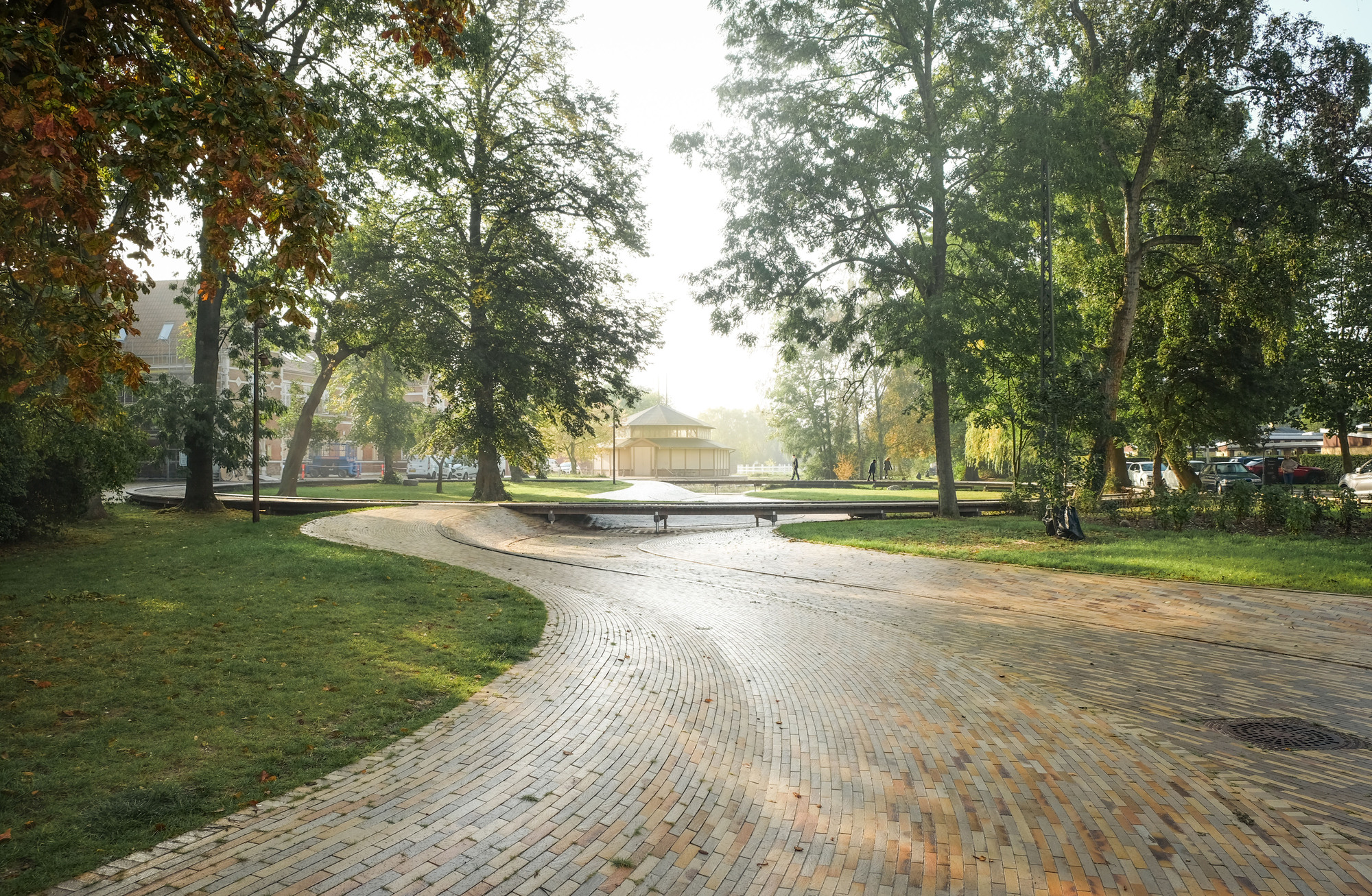 Patterned brick paving in a public plaza with trees and benches under soft morning mist
