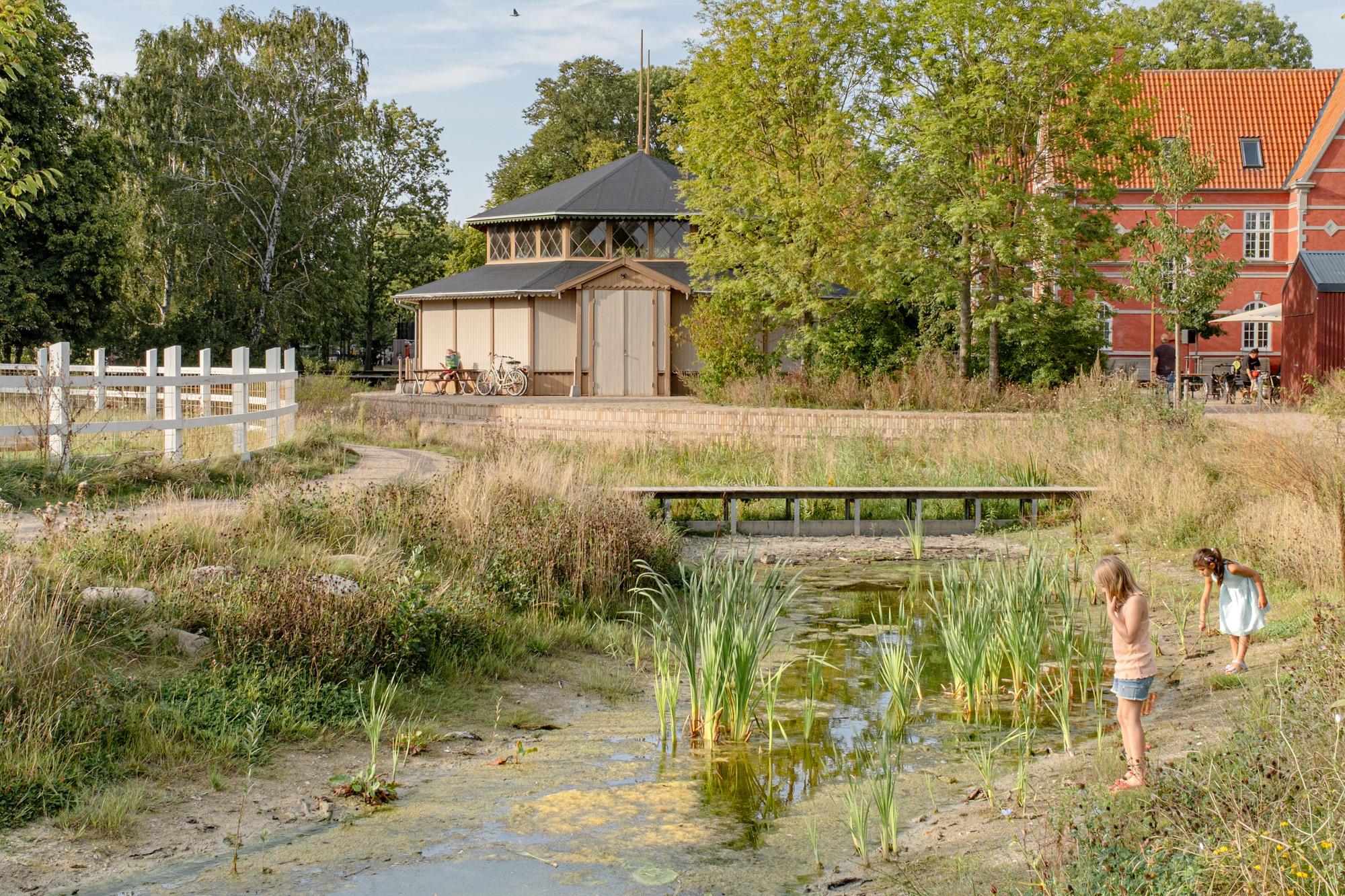 Octagonal pavilion with latticed timber walls and a dark pyramidal roof surrounded by shallow water pools