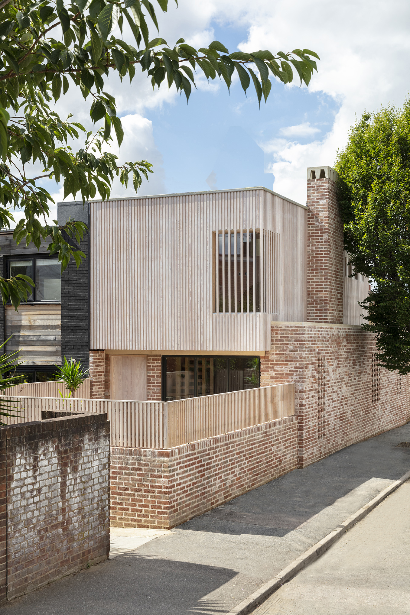 Street elevation showing corrugated metal volume with vertical slot window above perforated brick base and timber screening