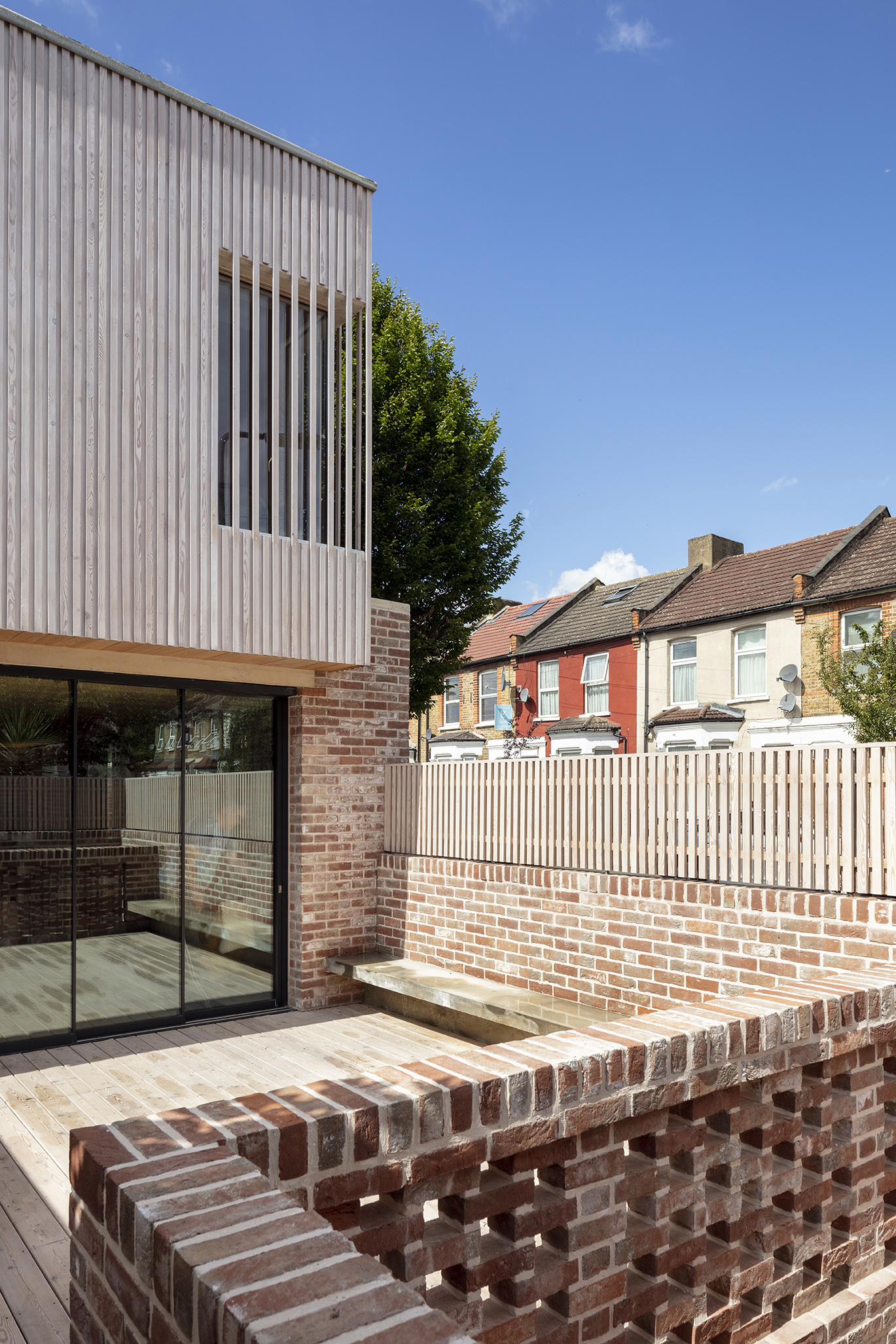 Timber deck terrace with perforated brick seating wall alongside painted stripe fence and neighboring houses