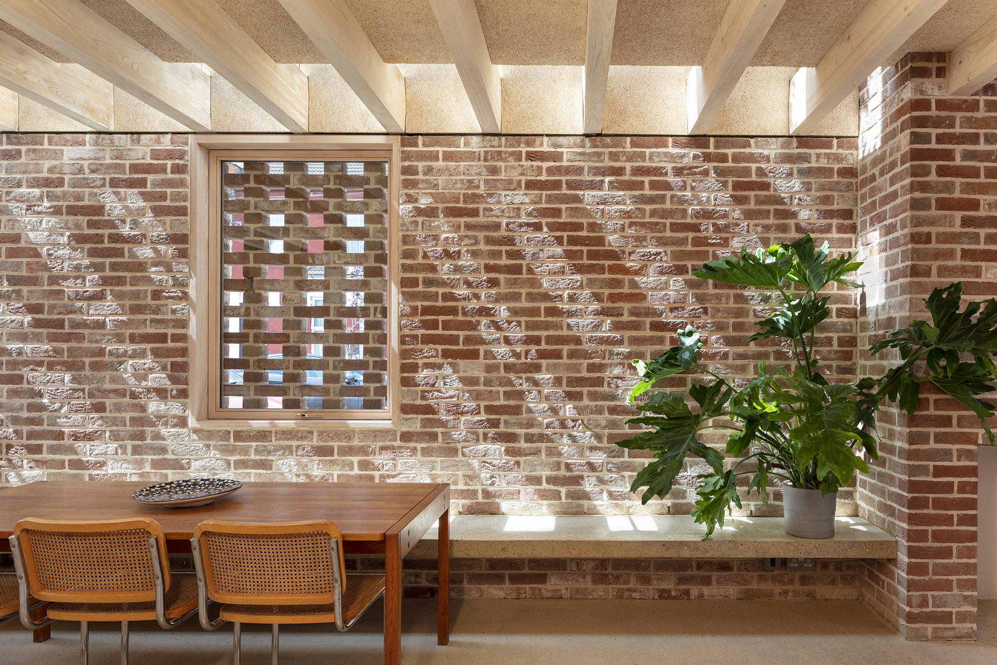 Interior dining area with exposed brick walls, timber ceiling beams and potted plants on a built-in concrete bench