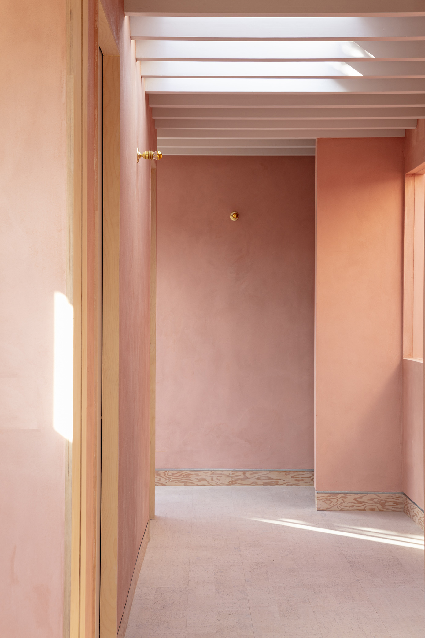 Doorway sequence through pink plastered rooms with plywood baseboards and overhead skylight slots