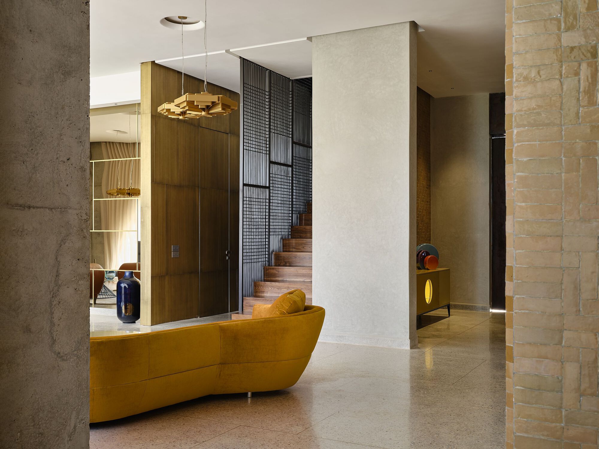 Interior hall with terrazzo floor, yellow upholstered seating, and dark metal mesh staircase screen