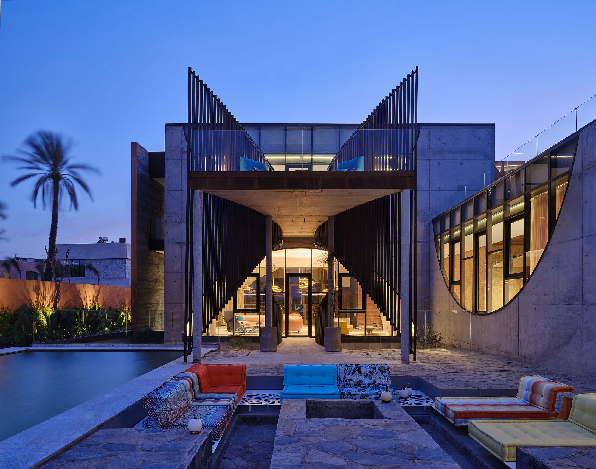 Rear courtyard with concrete volumes, arched opening, and vertical louvered towers illuminated at twilight