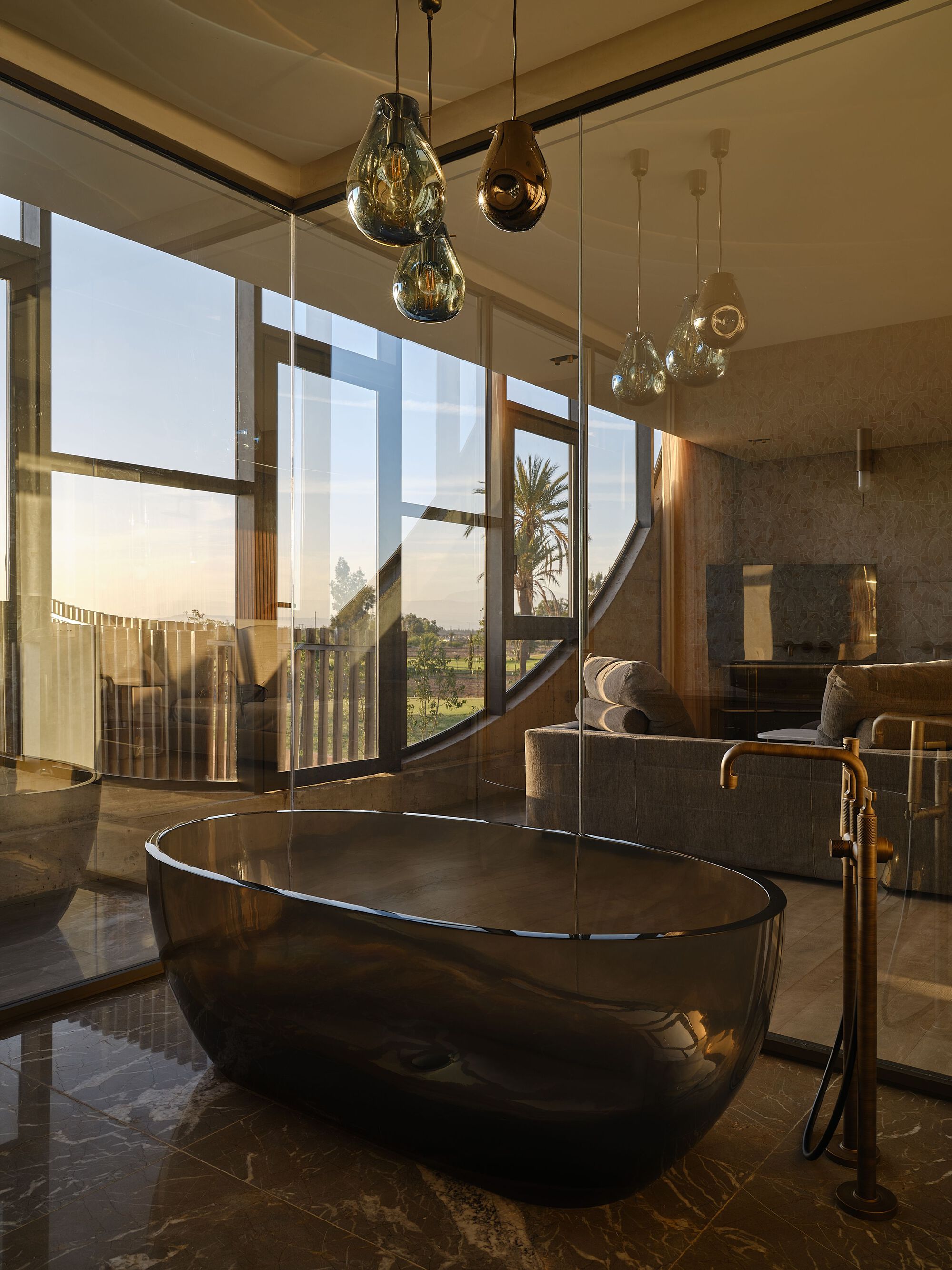 Freestanding black bathtub beneath sculptural glass pendants in golden hour light