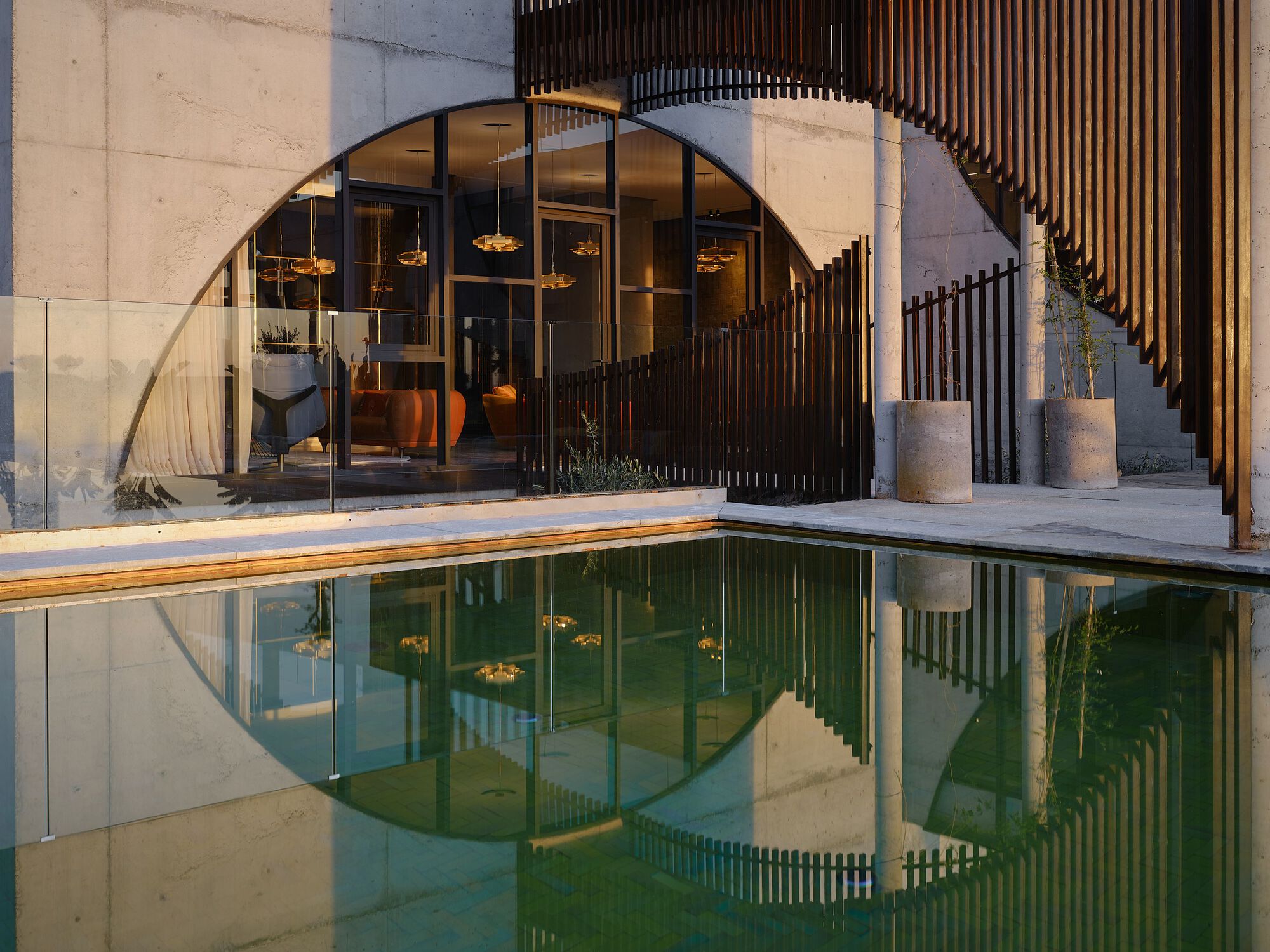 Arched entrance with vertical timber screens reflected in a still courtyard pool