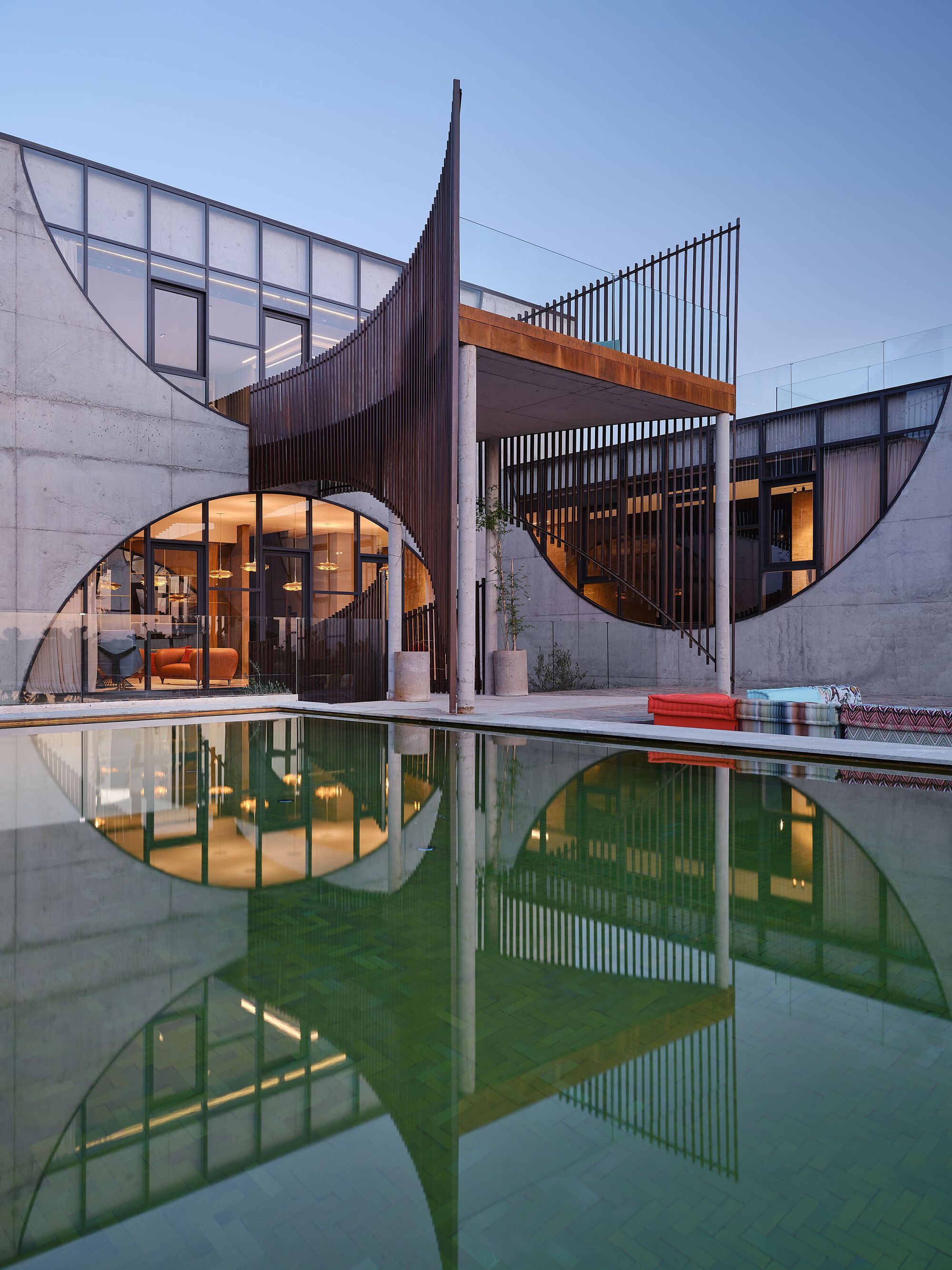 Curved timber screens and arched openings with concrete walls reflected in a courtyard pool