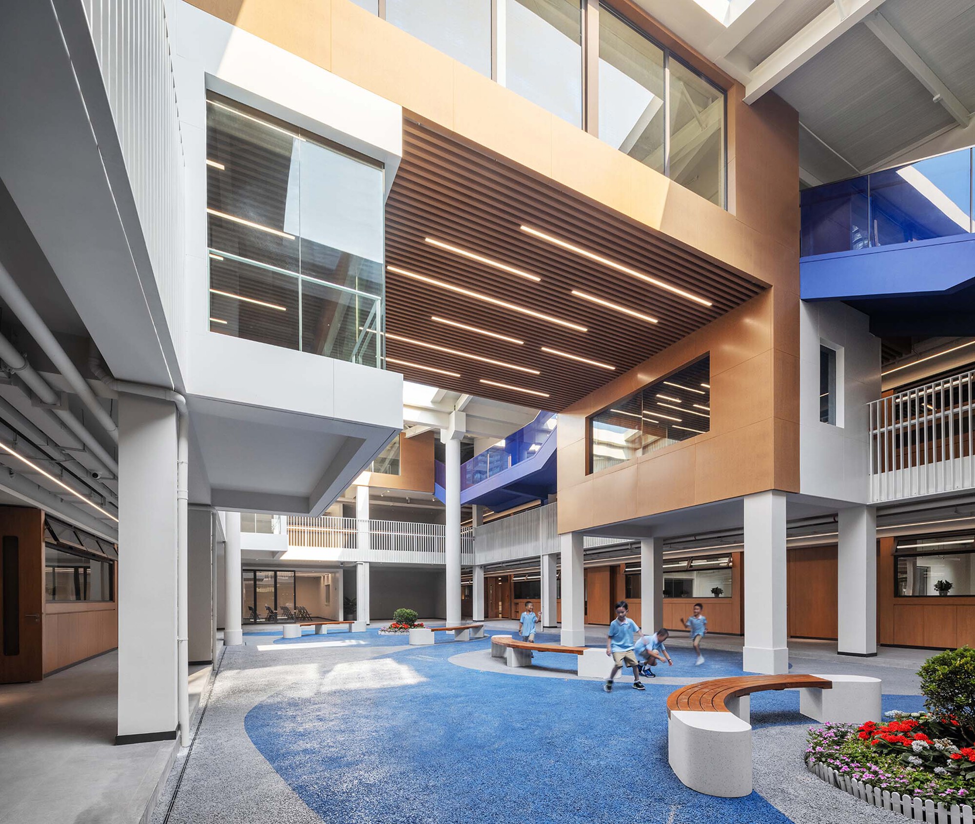 Multi-story atrium with timber-slat ceiling, blue carpet flooring, and curved seating where students gather