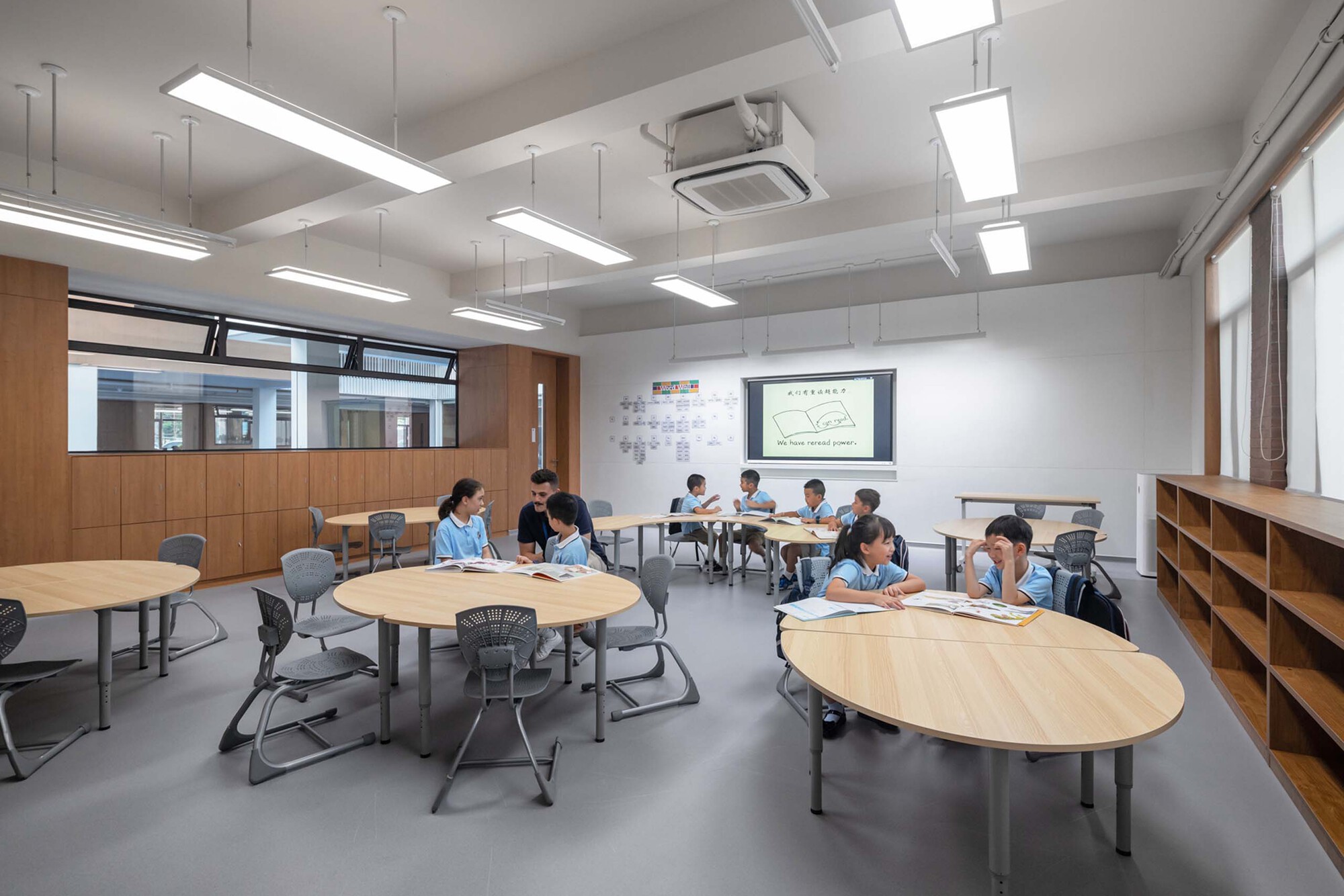 Classroom with oval tables, suspended linear lights, and students working in small groups