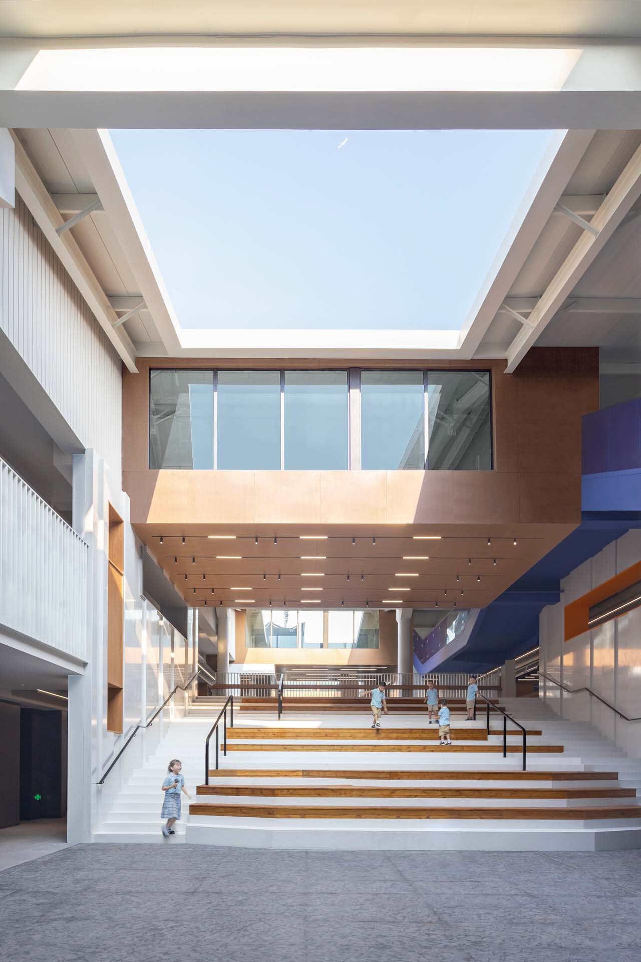 Interior staircase with perforated soffit and glass-enclosed bridge spanning the multi-level atrium