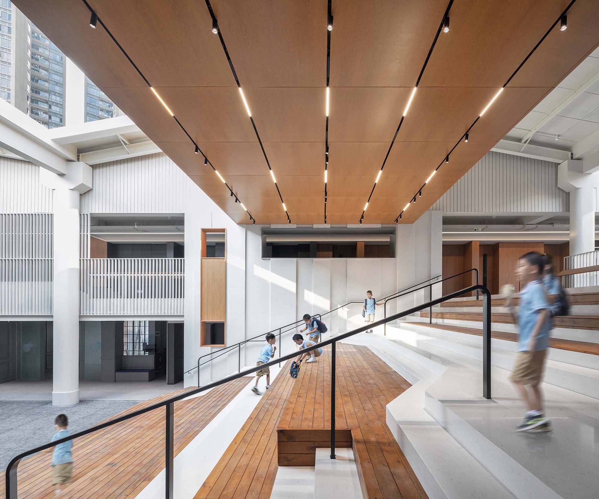 Interior atrium with timber and white tiered seating flanking a central ramp where students gather