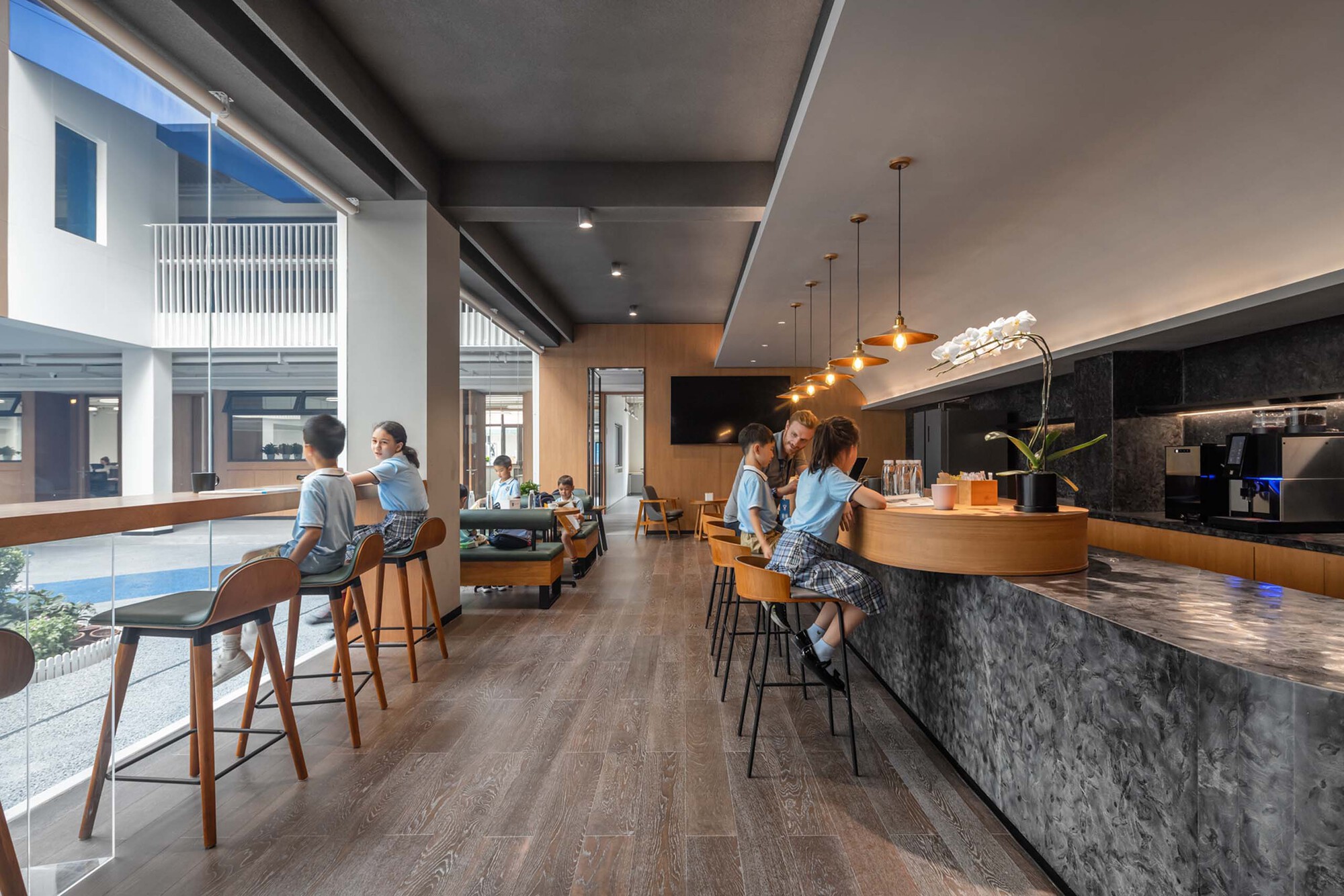Cafe space with marbled island counter and timber seating where students sit beneath a brown ceiling