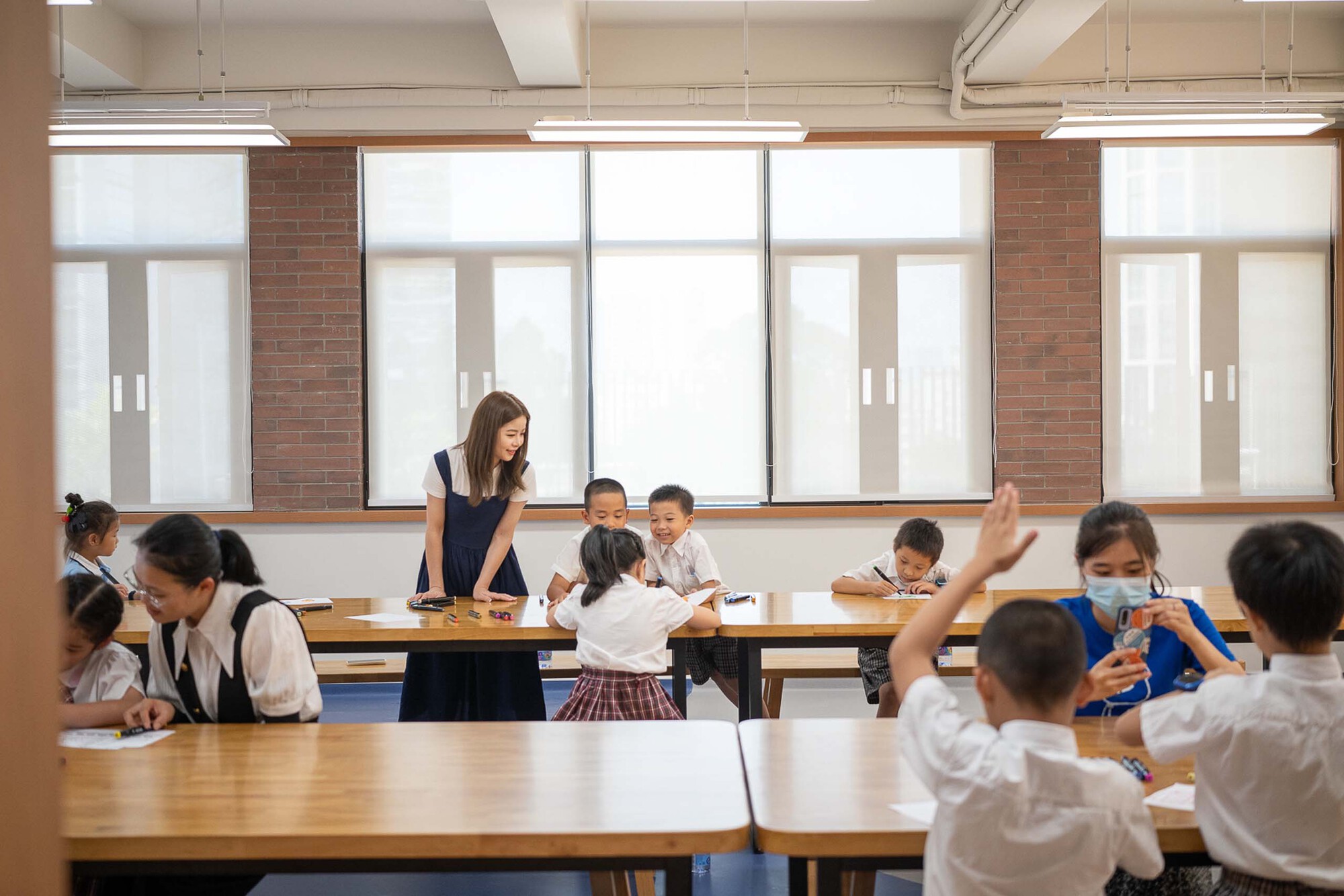 Classroom with large gridded windows and exposed brick piers where students work at wooden tables