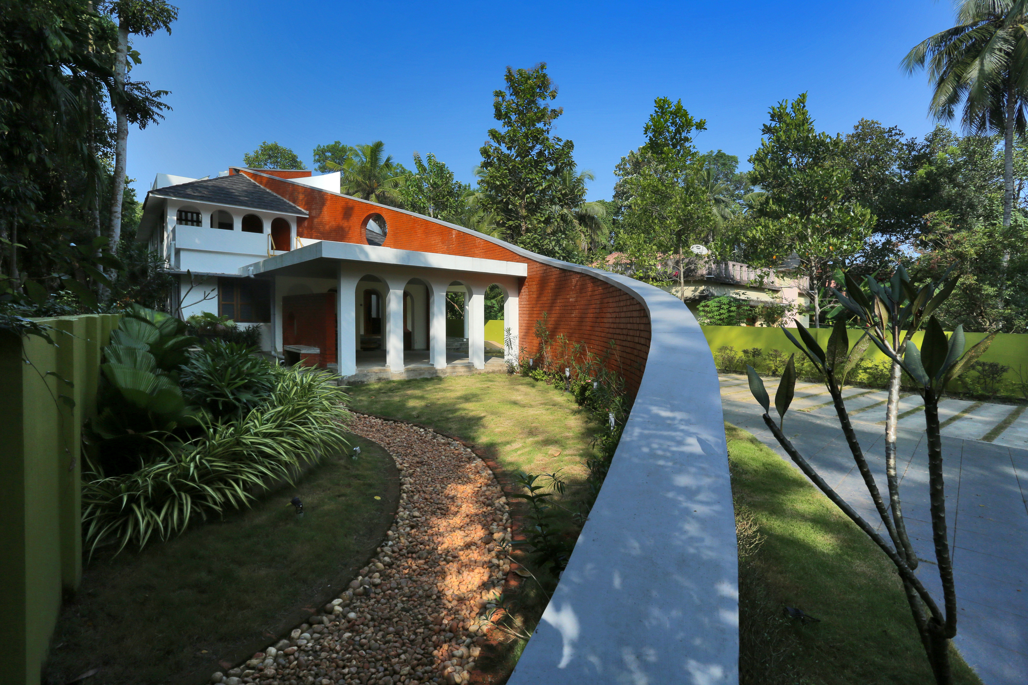 Exterior view of the curved red brick roof wall and white colonnade amid palm trees and lawn