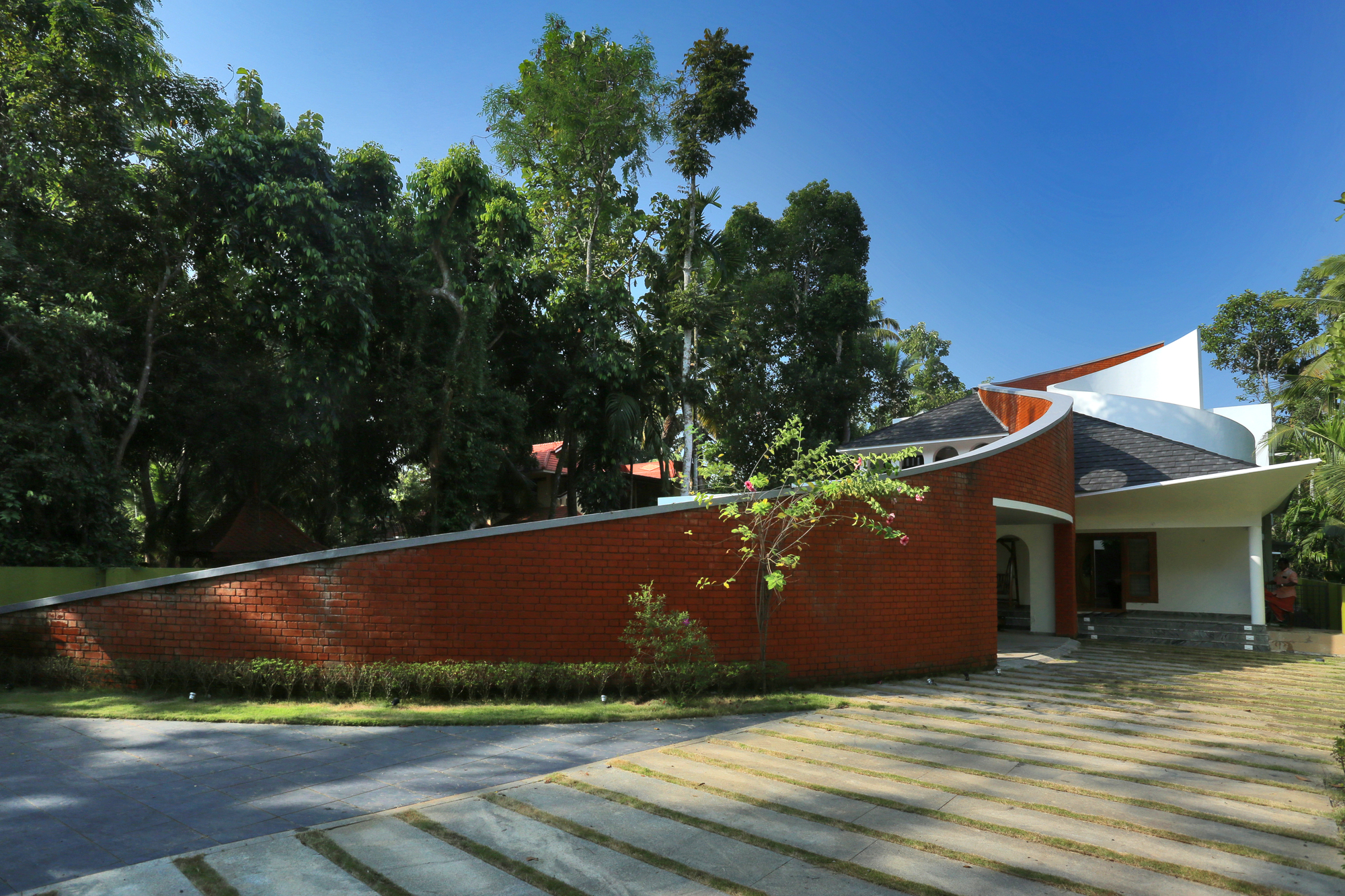 Entrance approach showing the long red brick wall and striped stone paving under a clear blue sky