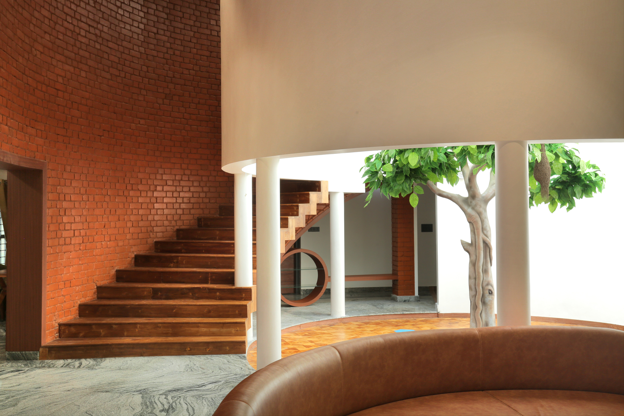 Interior staircase with timber treads against a red brick wall opening to a courtyard with a potted tree