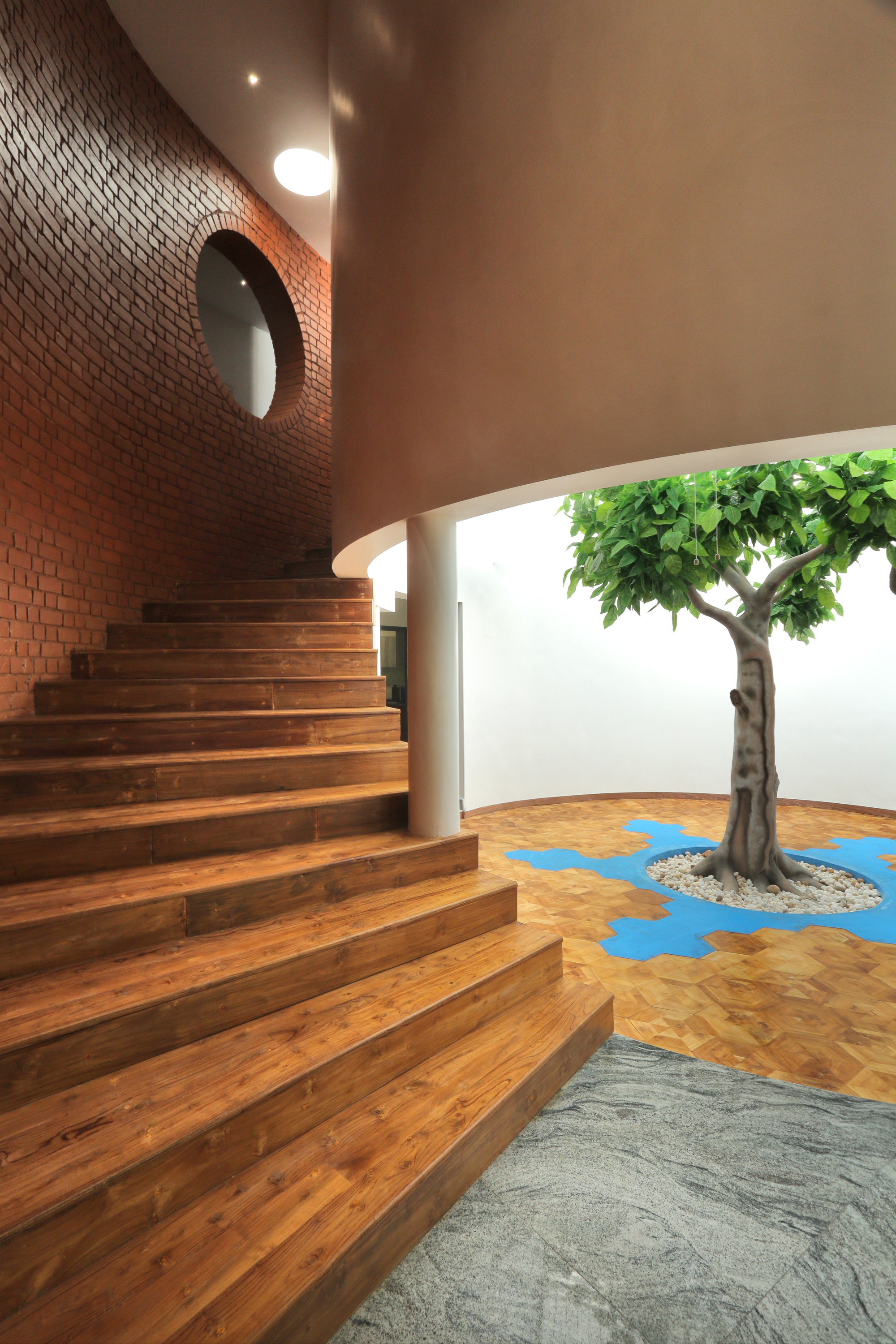 Timber stair rising along the curved brick wall beside a courtyard with tree and patterned floor inlay