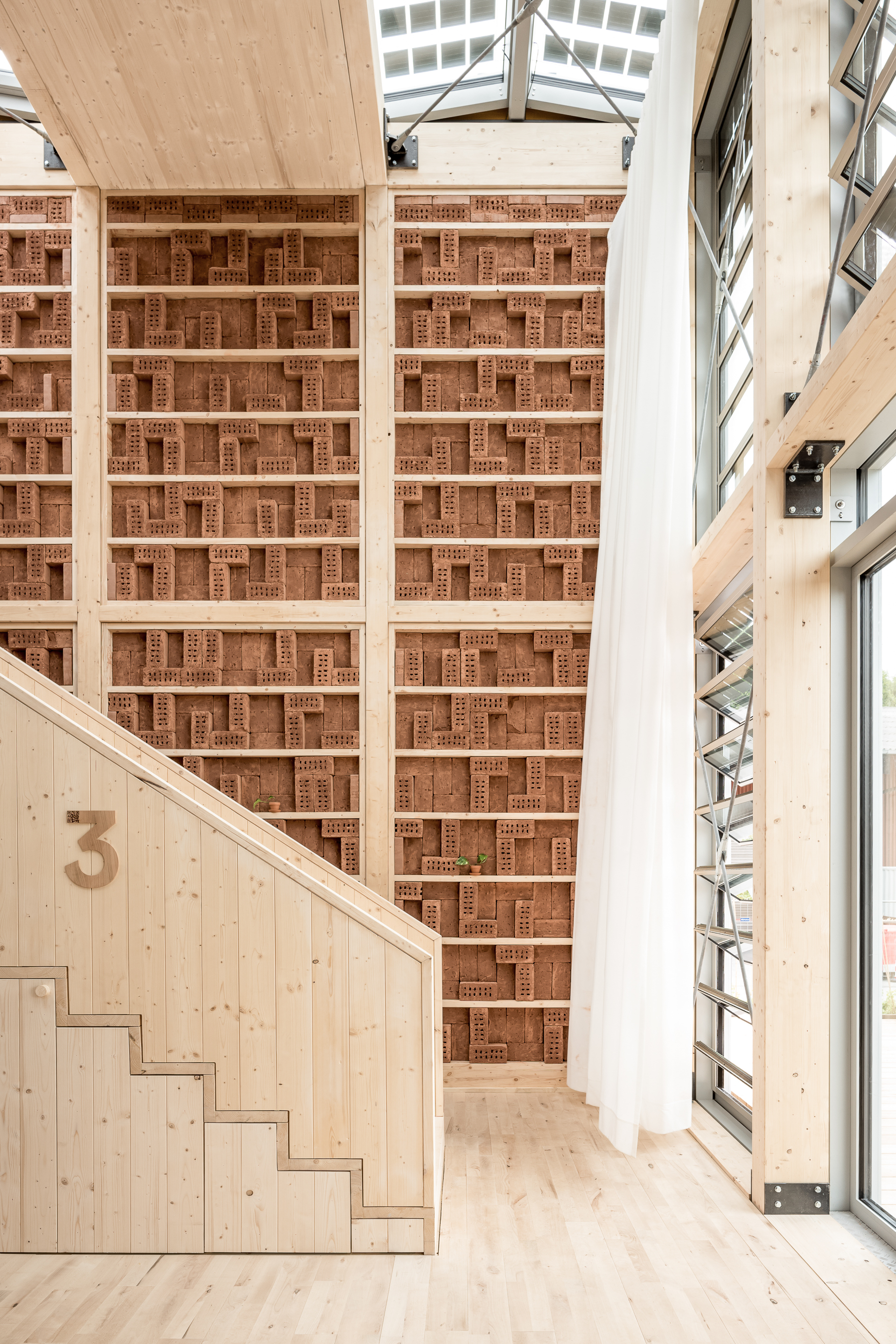 Double-height space with perforated brick wall, timber staircase and triangular glazed clerestory above