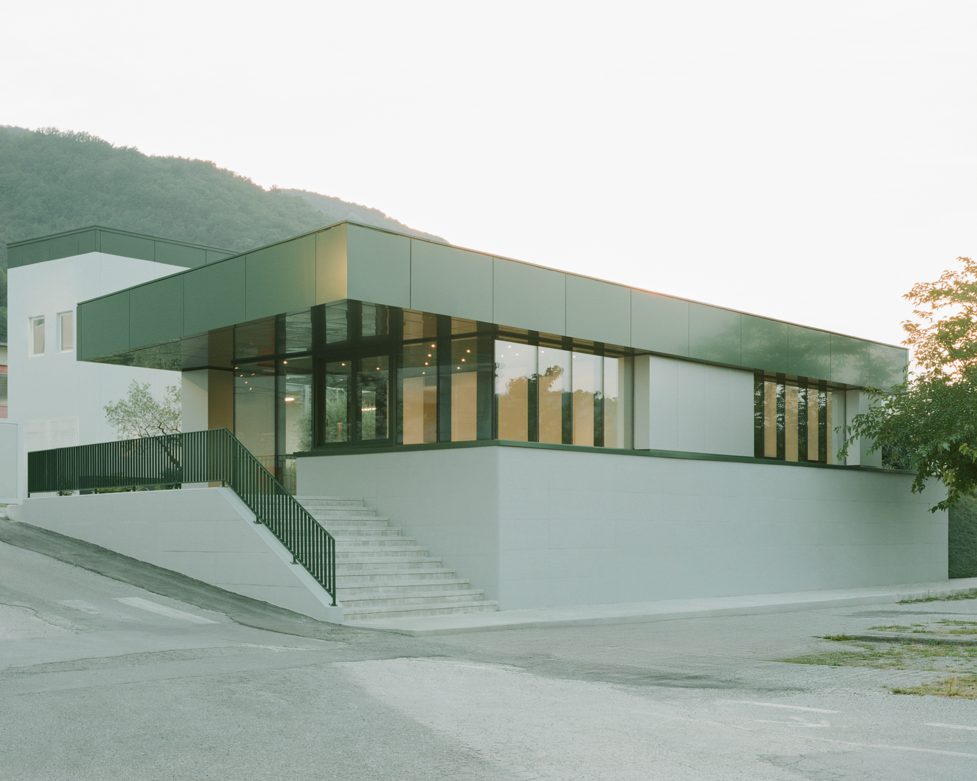Corner view of the elevated entrance plaza and glazed facade with forested hillside behind