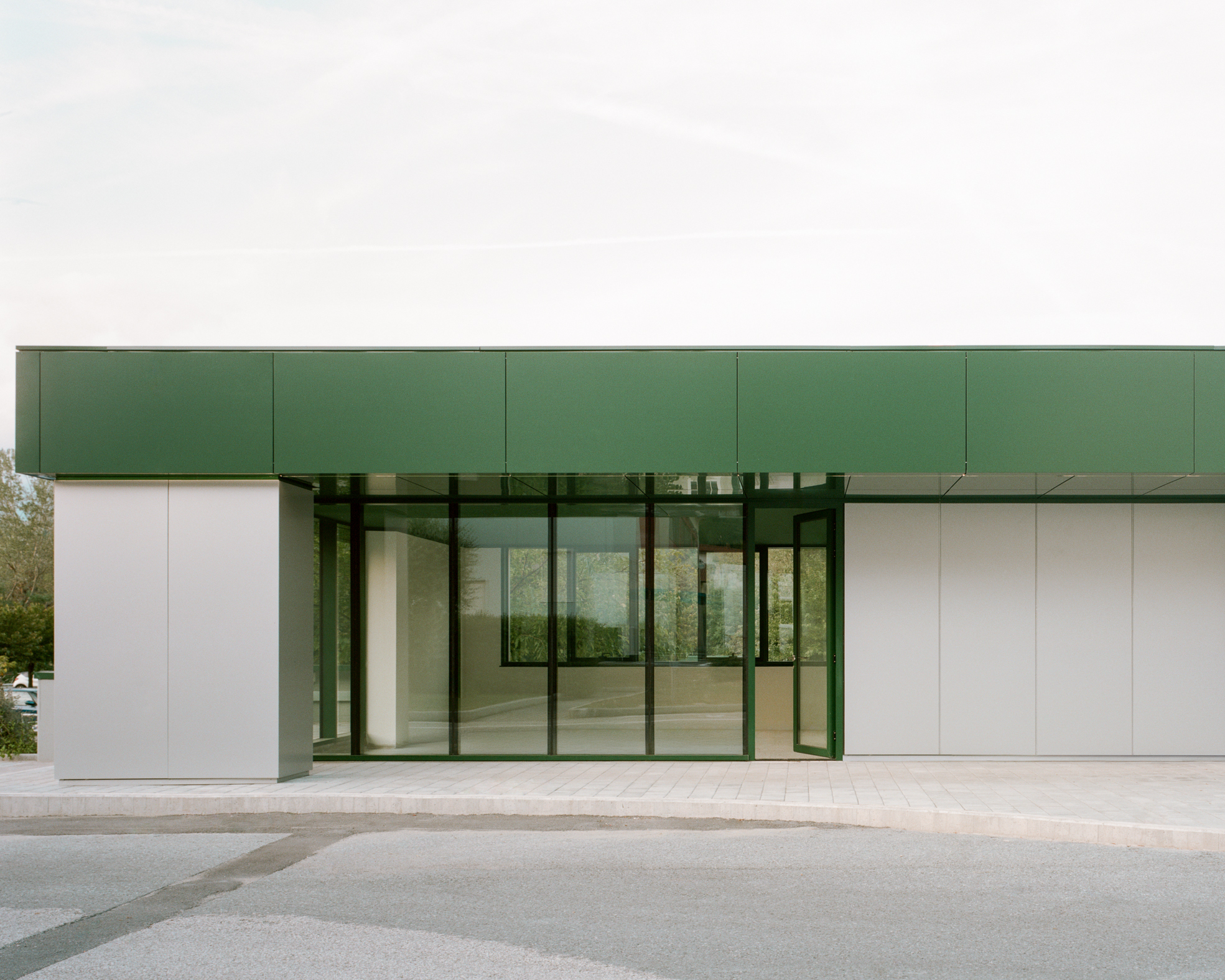 Recessed glass entry portal framed by white panels and green metal canopy under overcast sky