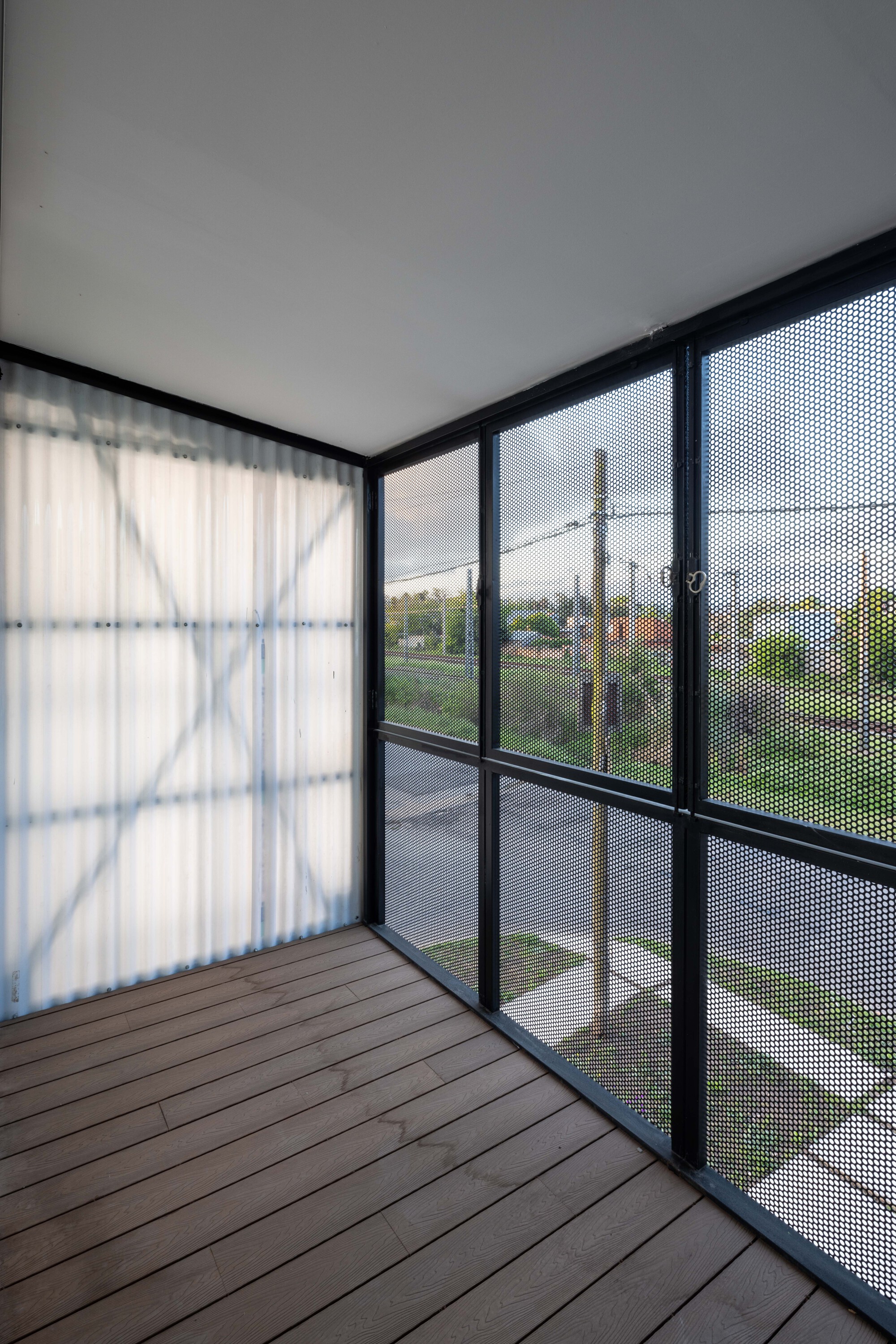 Balcony with timber decking enclosed by black-framed perforated mesh screens overlooking a suburban street
