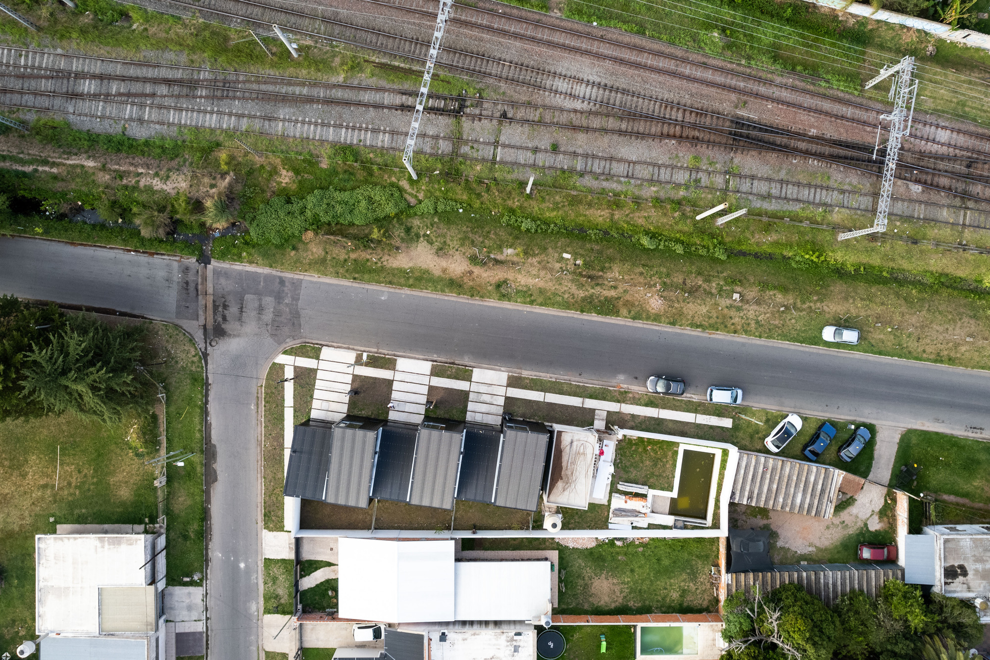 Aerial view showing the stepped arrangement of four townhouse units with white and corrugated metal roofs alongside railway tracks