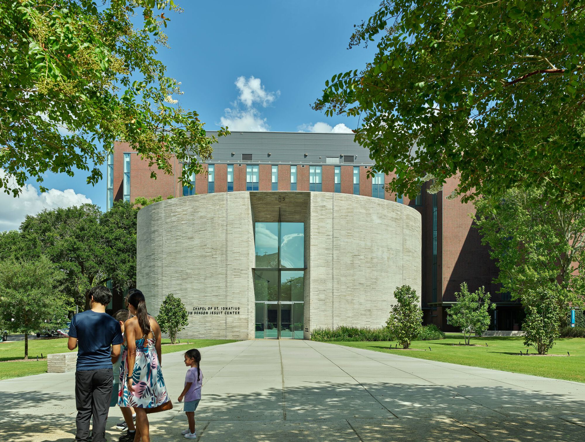 Curved grey brick facade with vertical glazing as visitors approach along a concrete path