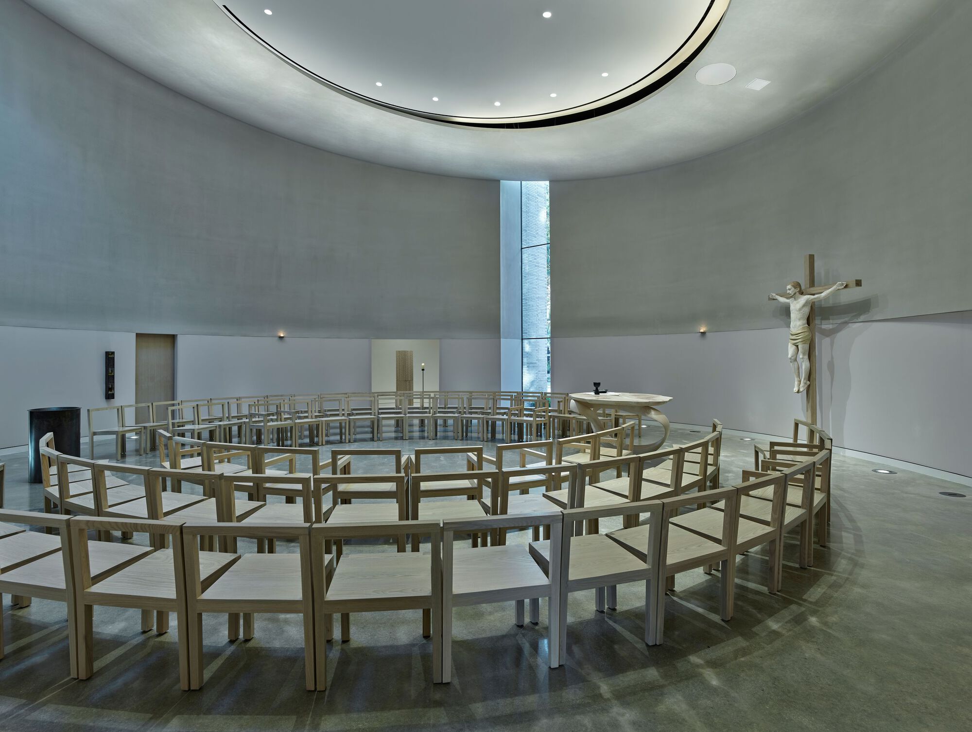 Circular chapel interior with concentric timber pews and a vertical light slot overhead
