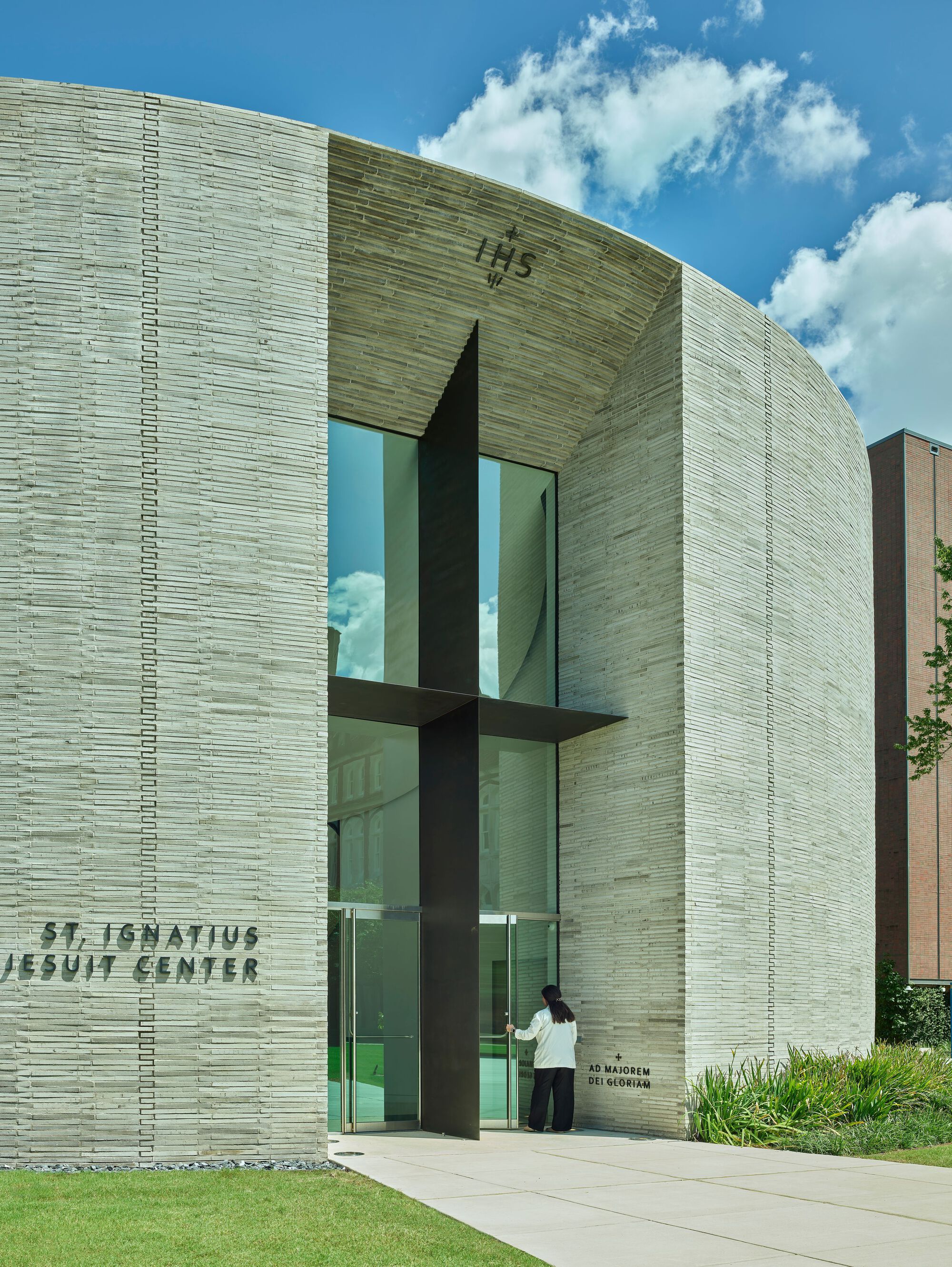Glazed cross cutting through the layered grey brick entrance facade on a sunny day